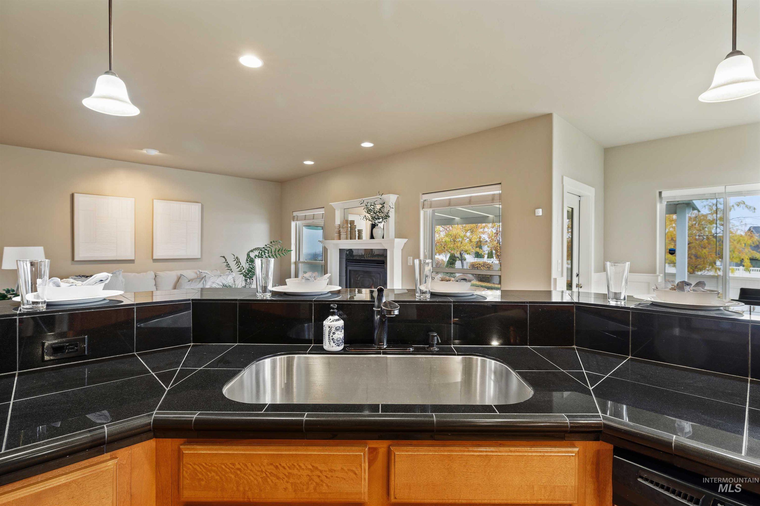 Kitchen featuring hanging light fixtures, open floor plan, recessed lighting, brown cabinetry, and a glass covered fireplace