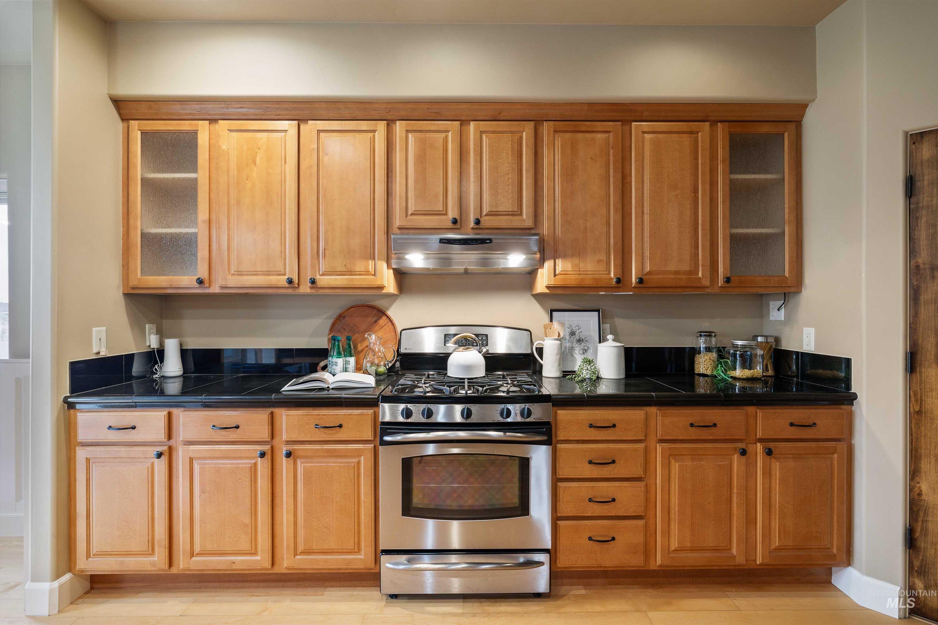Kitchen featuring glass insert cabinets, stainless steel range with gas cooktop, extractor fan, and brown cabinetry