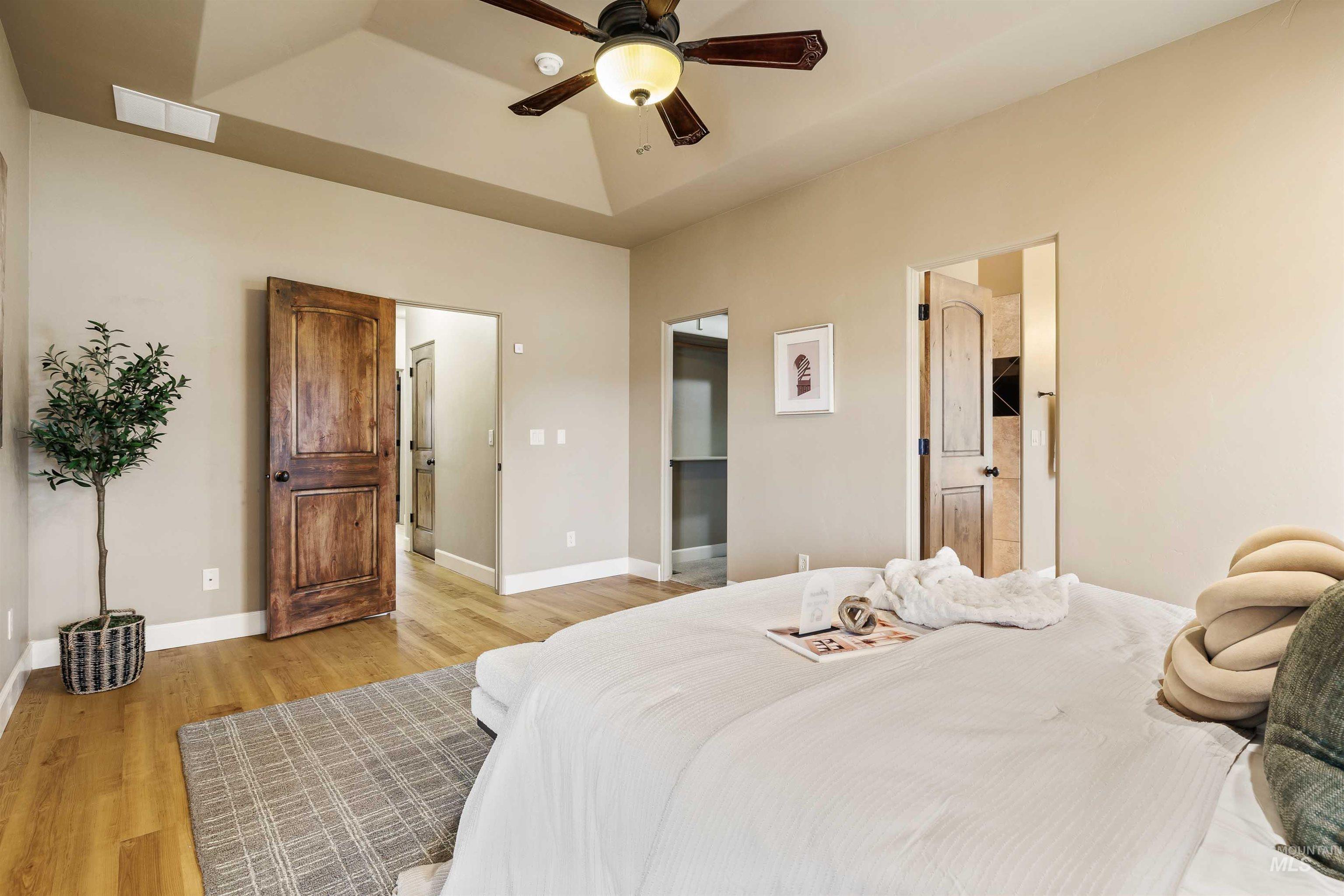Bedroom featuring wood finished floors, ceiling fan, a raised ceiling, and connected bathroom