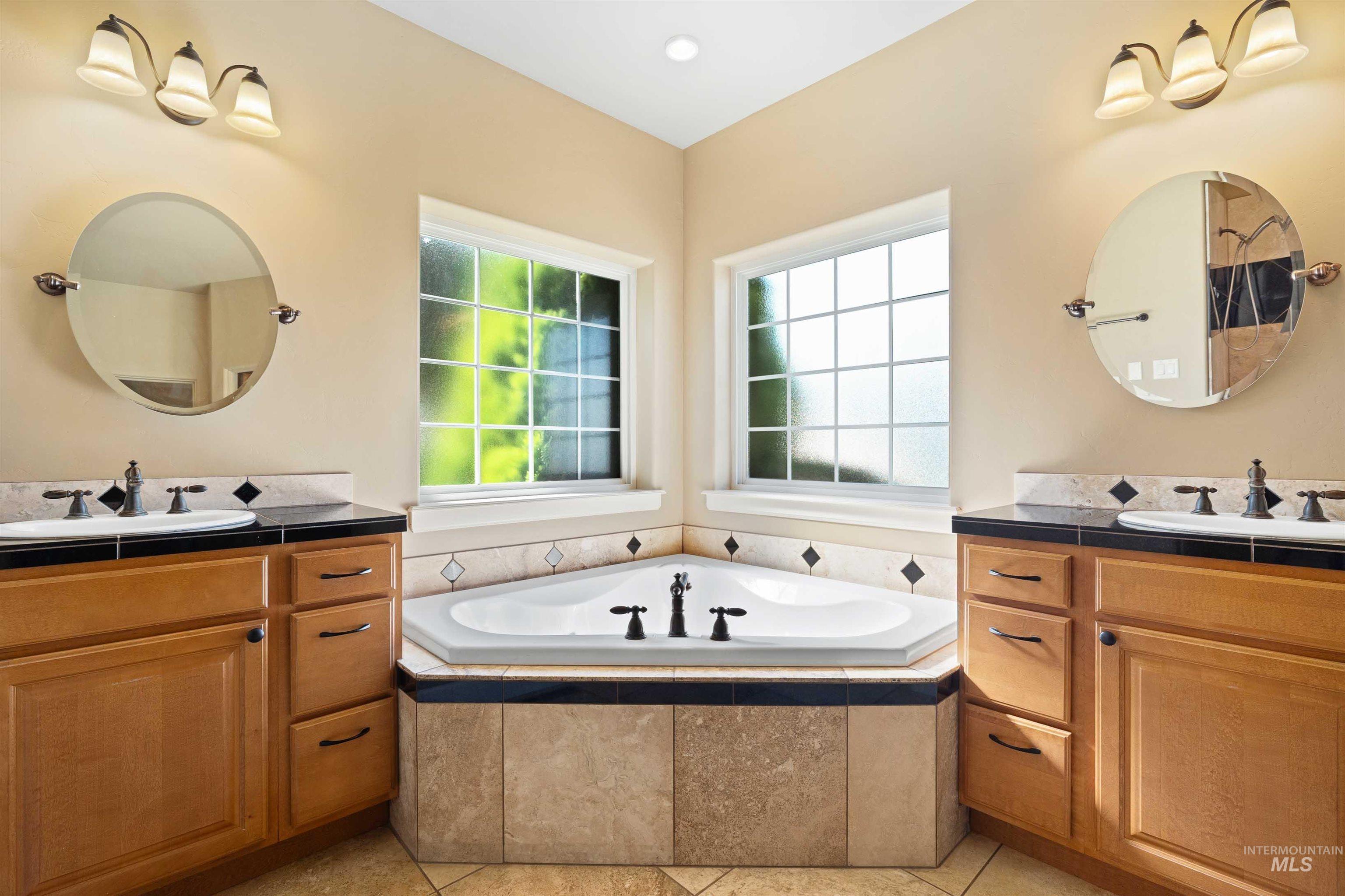 Bathroom featuring a bath, two vanities, and light tile patterned floors