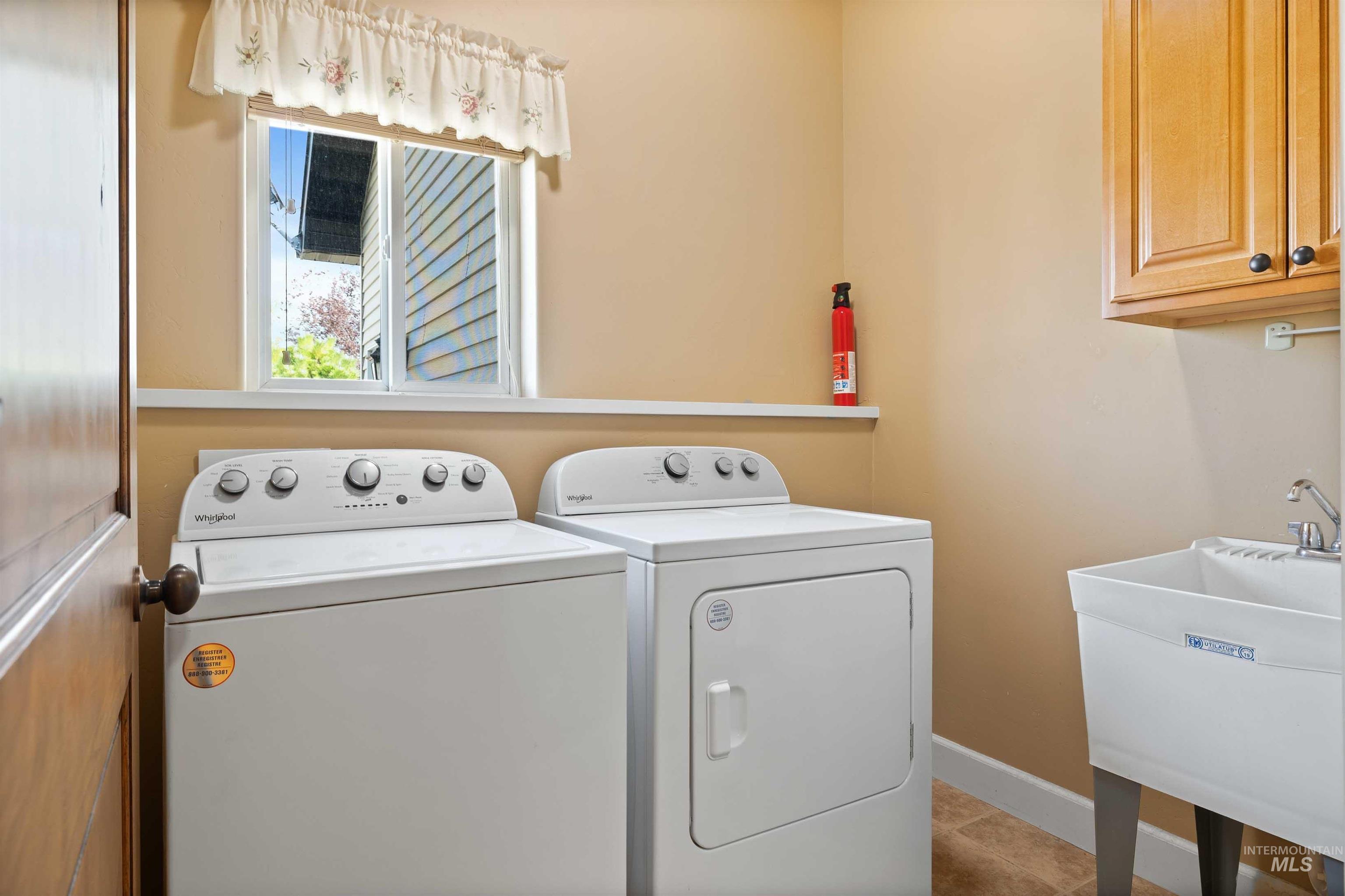 Laundry room with independent washer and dryer, light tile patterned floors, and cabinet space