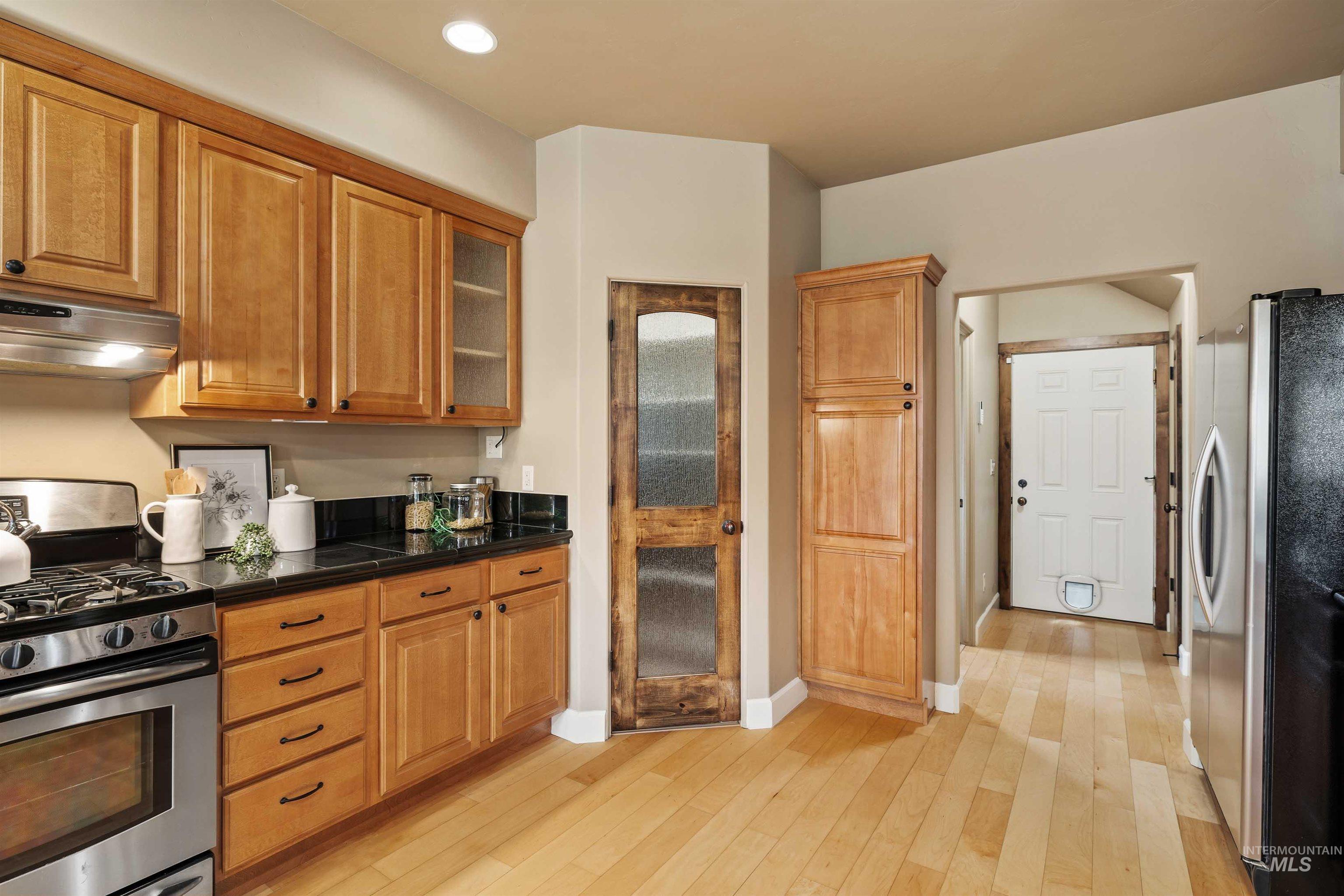 Kitchen with stainless steel appliances, light wood-style floors, ventilation hood, brown cabinetry, and recessed lighting