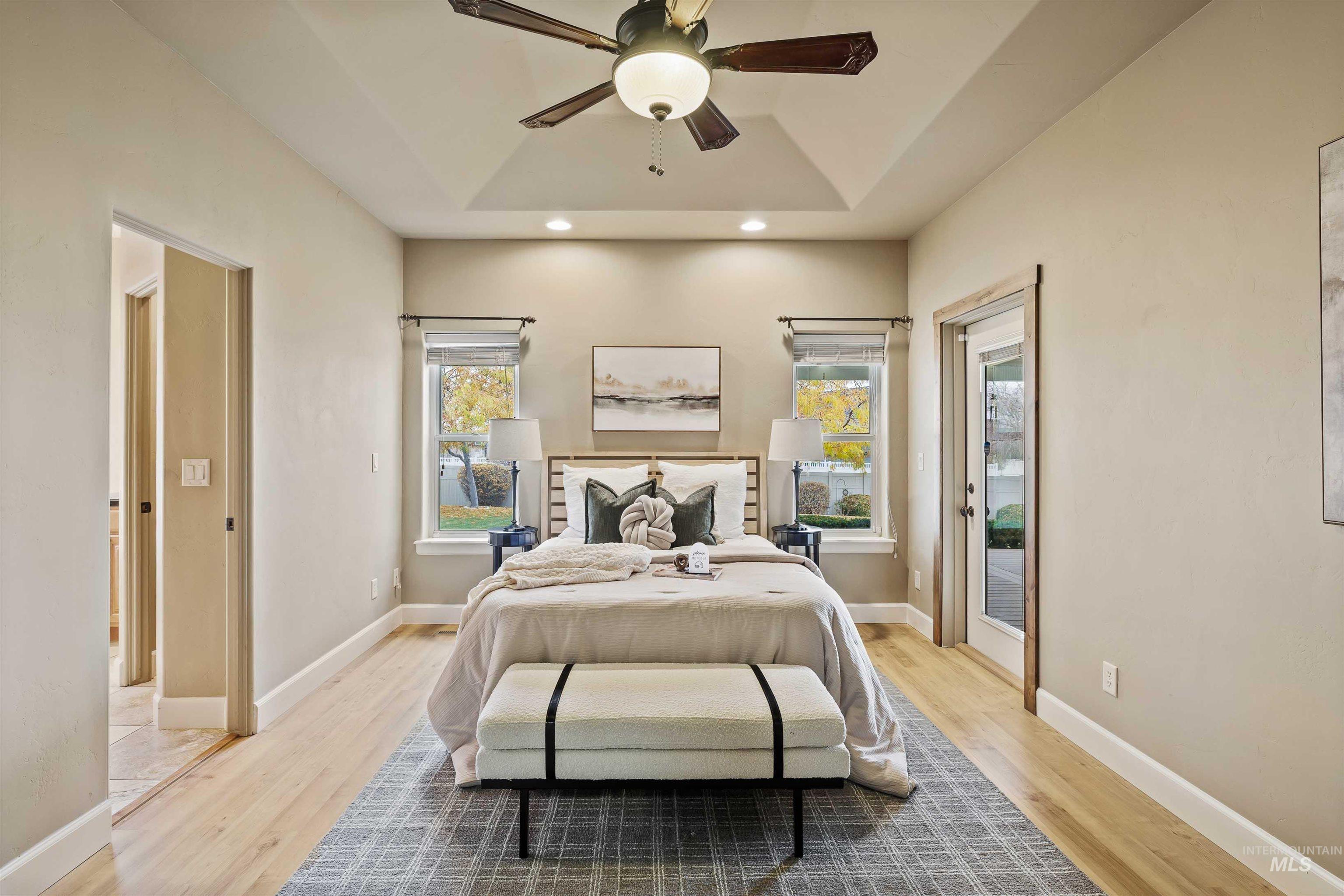 Bedroom featuring access to exterior, multiple windows, light wood-type flooring, and a tray ceiling