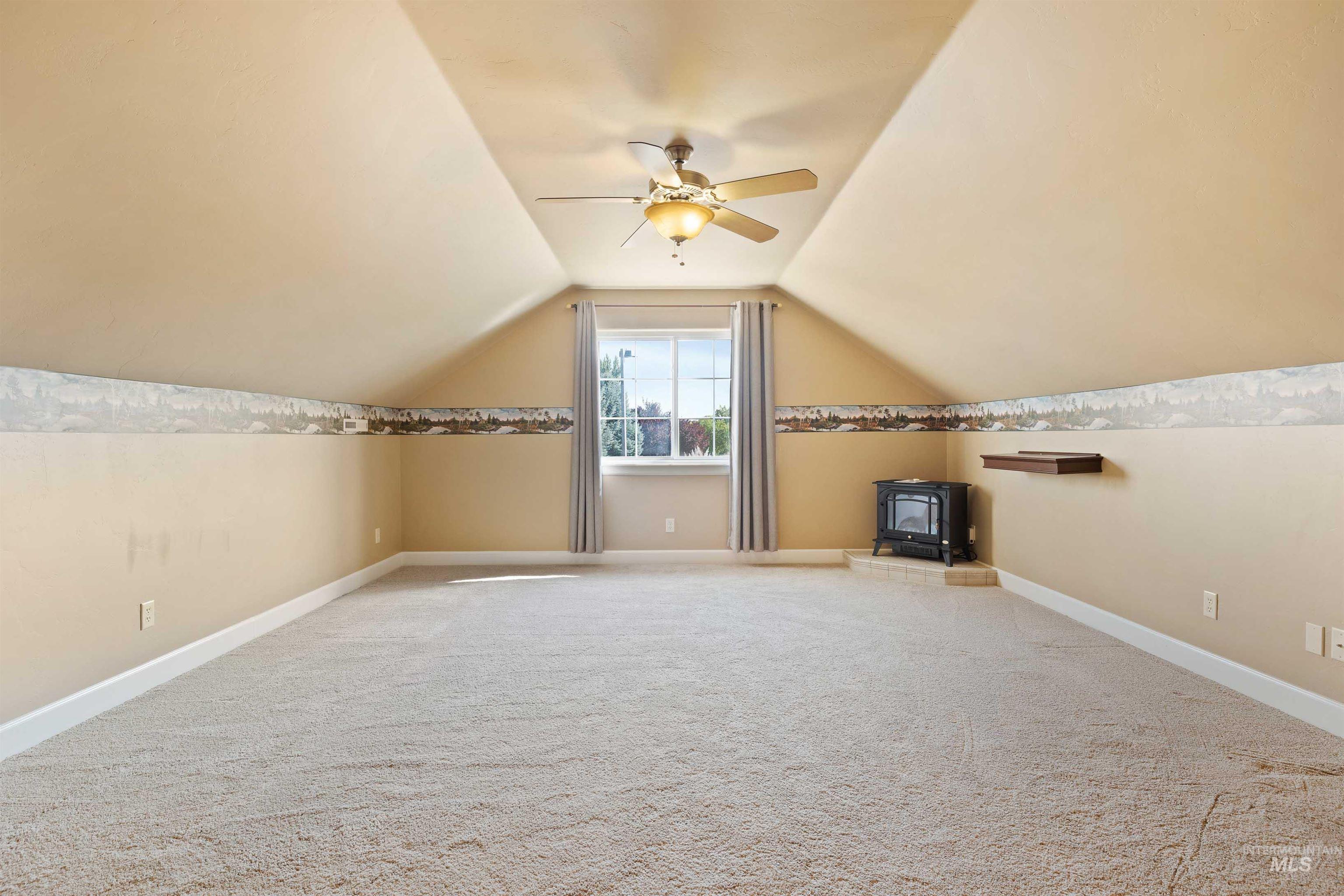 Additional living space with a wood stove, lofted ceiling, light colored carpet, and ceiling fan