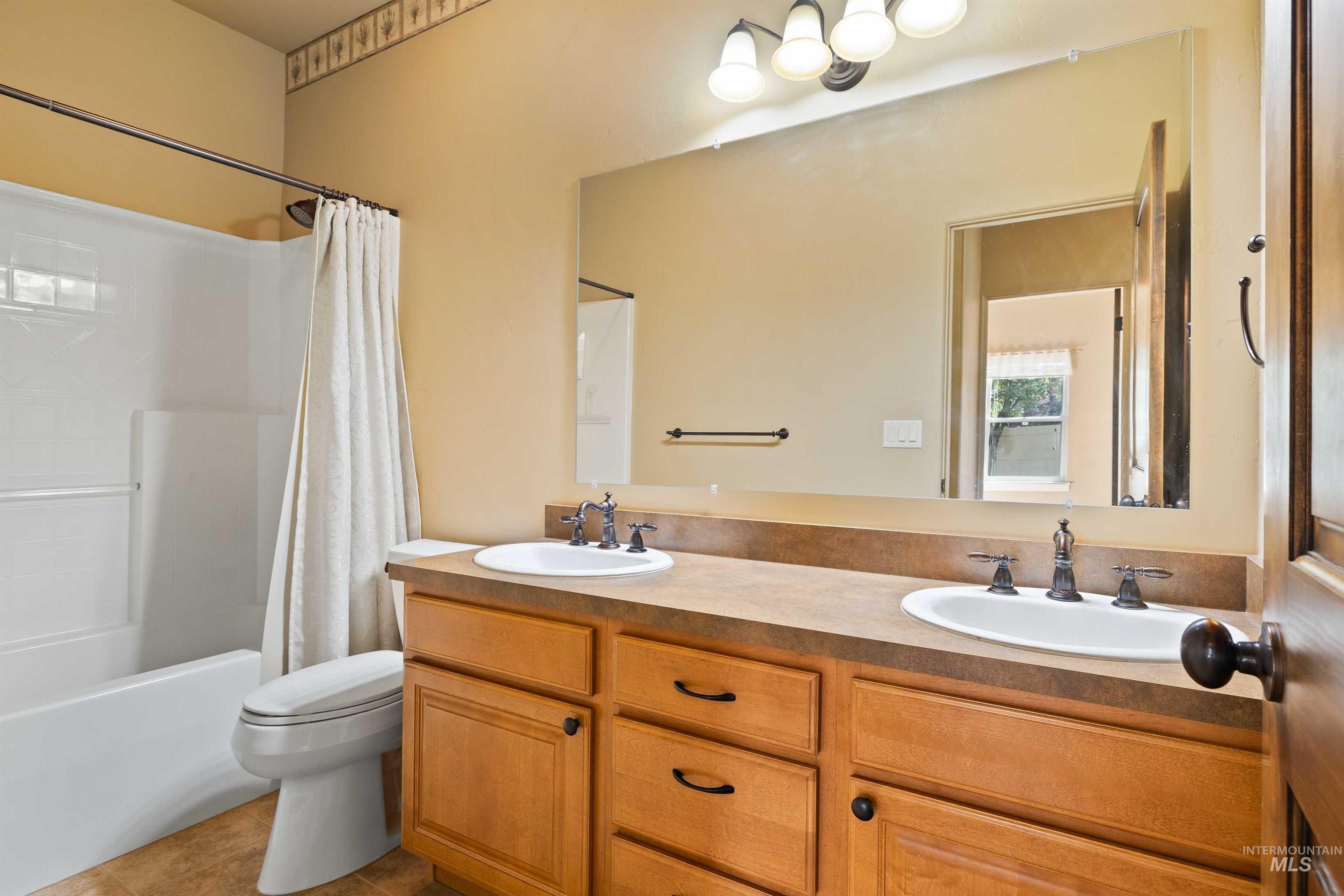 Bathroom with shower / bathtub combination with curtain, double vanity, and light tile patterned floors