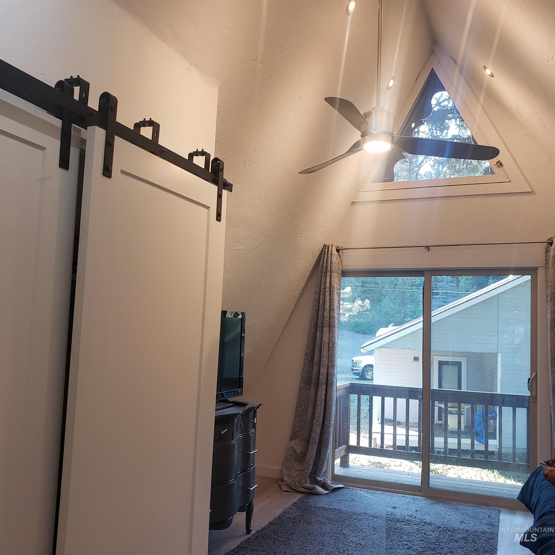 Doorway with ceiling fan, wood finished floors, a textured wall, and vaulted ceiling