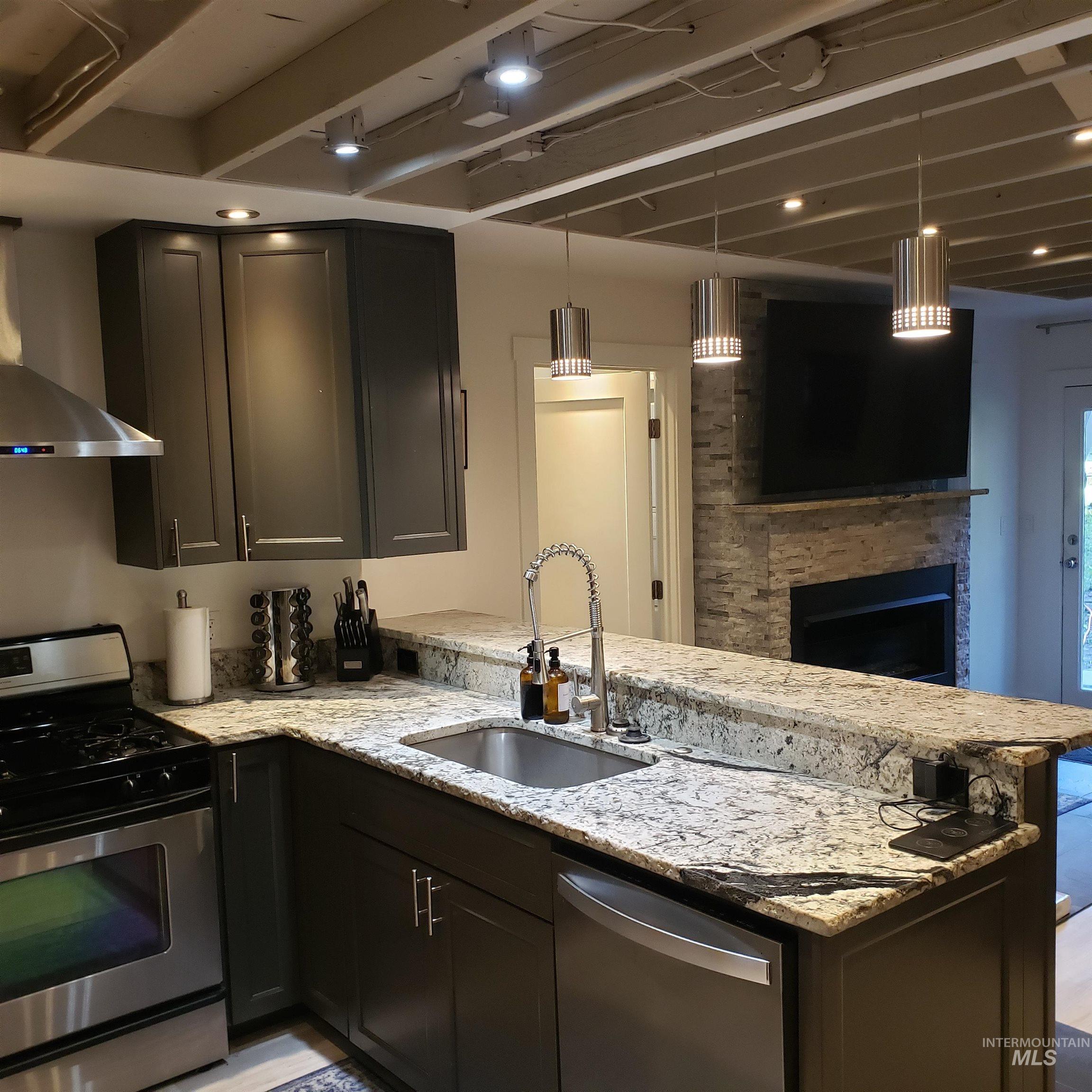 Kitchen featuring stainless steel appliances, pendant lighting, light stone counters, wall chimney range hood, and a peninsula