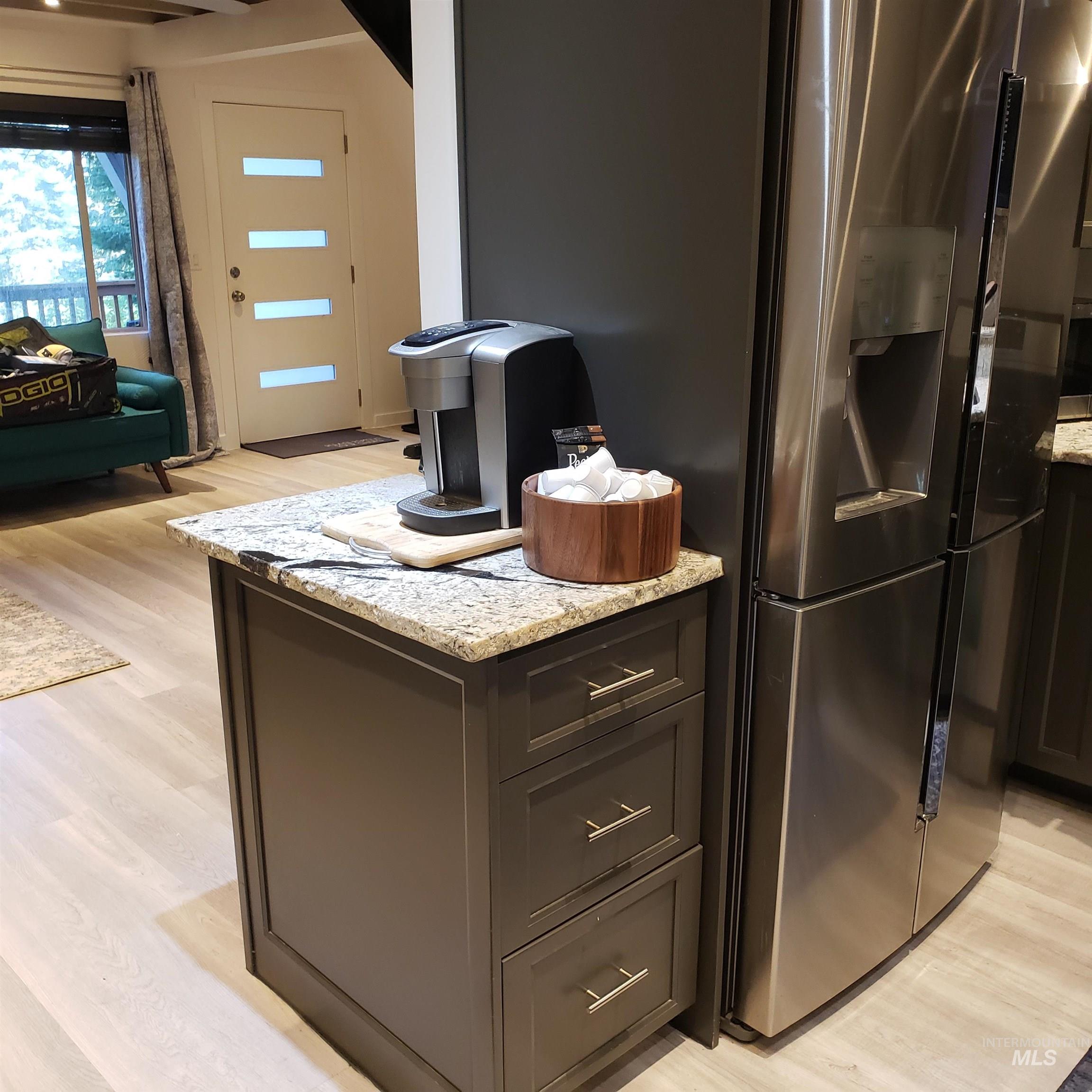 Kitchen with light wood-style floors, light stone countertops, stainless steel refrigerator with ice dispenser, and open floor plan
