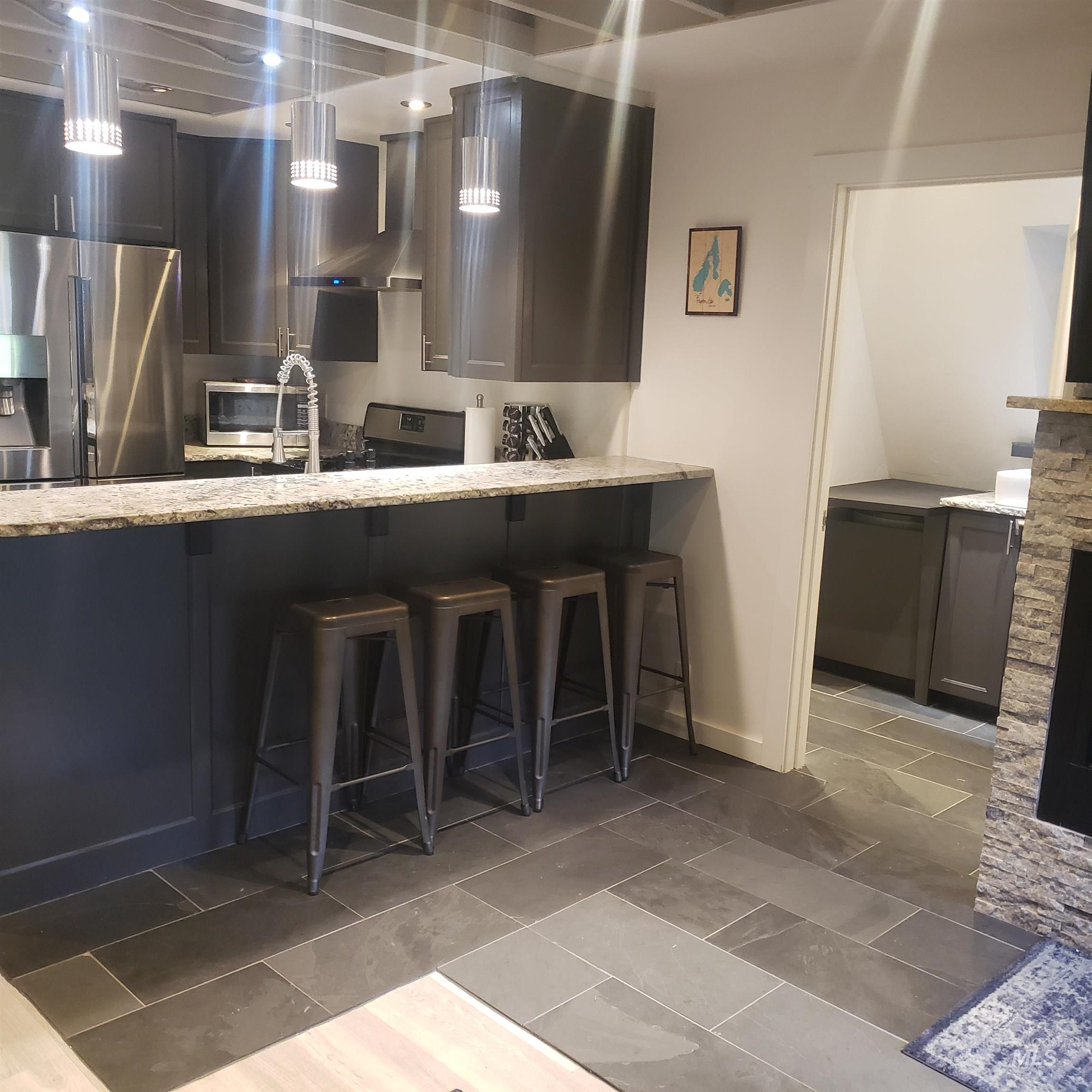Kitchen with a breakfast bar, appliances with stainless steel finishes, light stone countertops, and hanging light fixtures