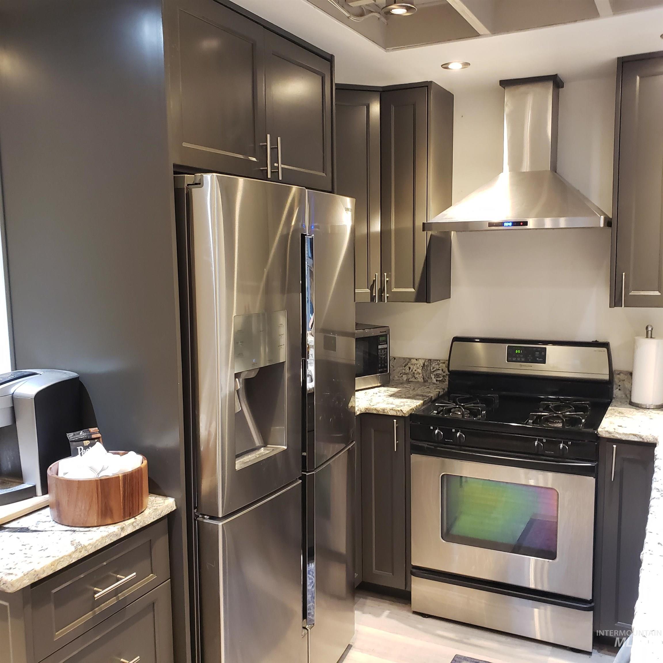 Kitchen with stainless steel appliances, light stone countertops, and wall chimney range hood