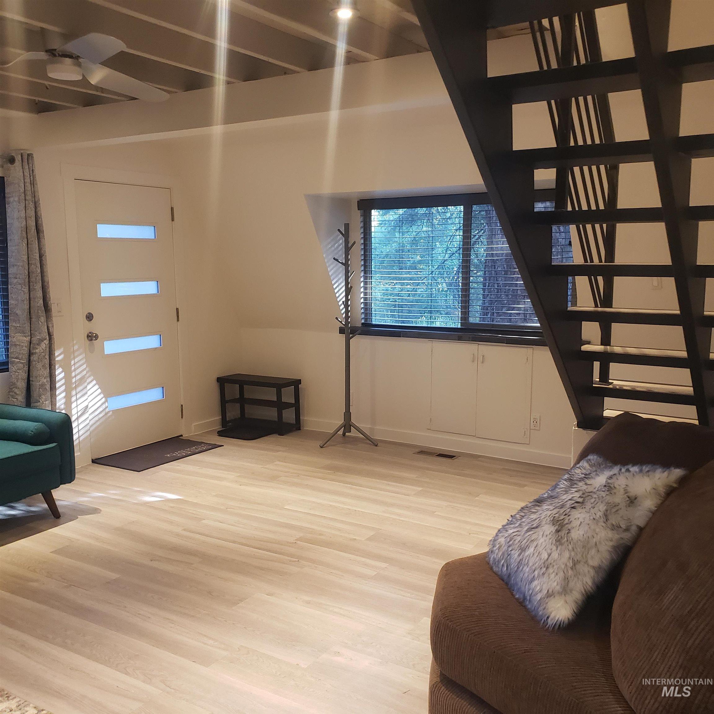 Living room featuring light wood-style flooring, a ceiling fan, and stairs