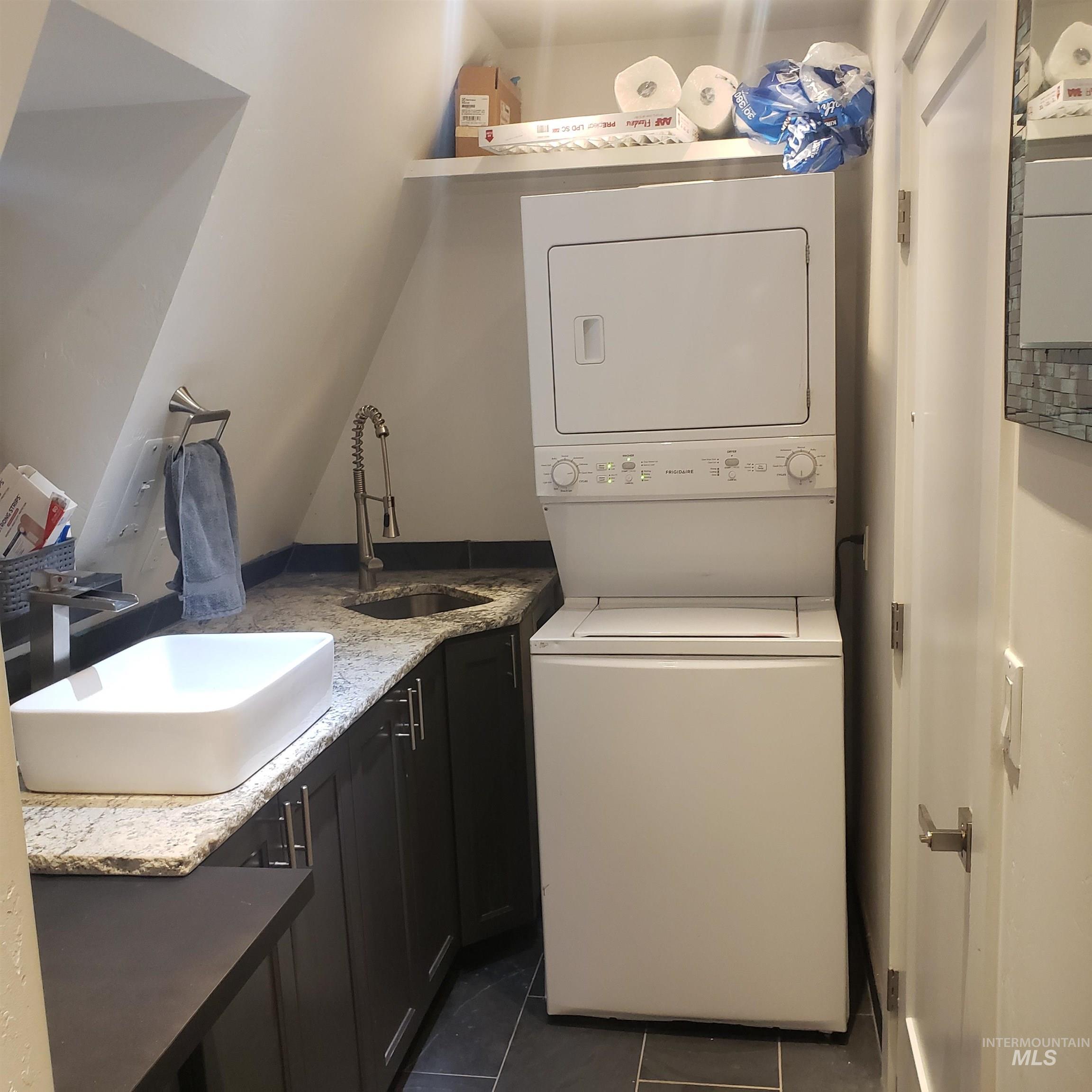Laundry area with stacked washer / dryer, dark tile patterned floors, and cabinet space