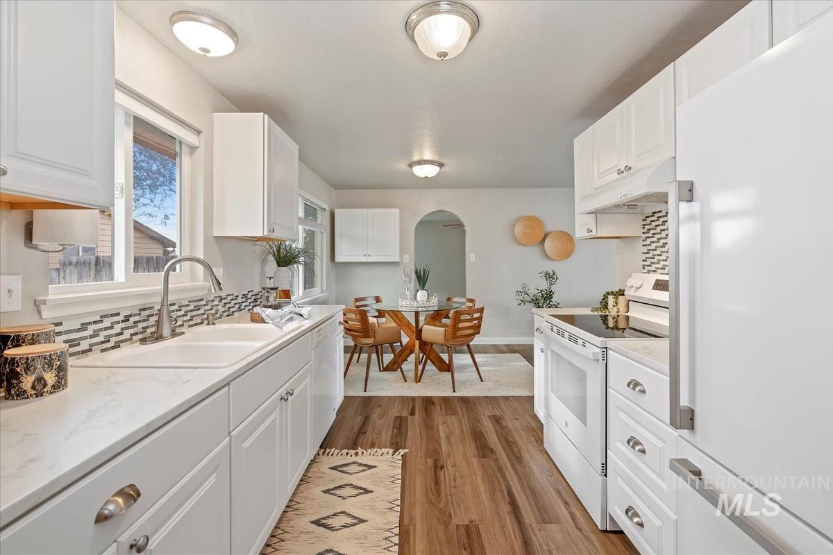 Kitchen with white appliances, white cabinets, arched walkways, under cabinet range hood, and light wood-type flooring