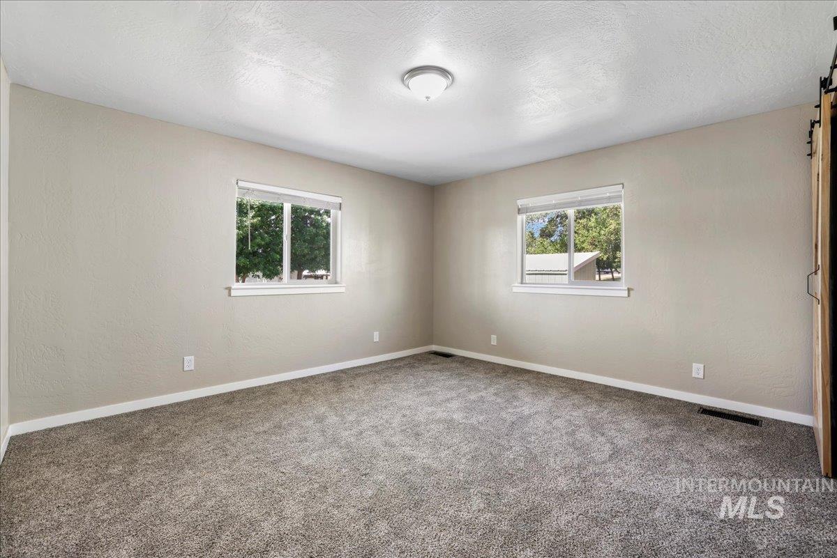 Carpeted spare room with a barn door, plenty of natural light, and a textured ceiling