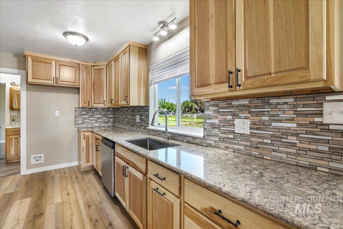 Kitchen featuring dishwasher, light wood finished floors, light stone countertops, tasteful backsplash, and light brown cabinetry