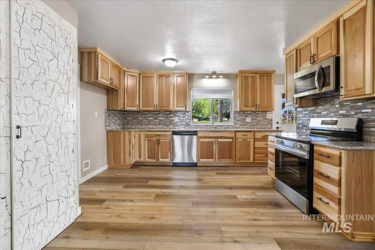 Kitchen with stainless steel appliances, light wood-style floors, decorative backsplash, and a textured ceiling