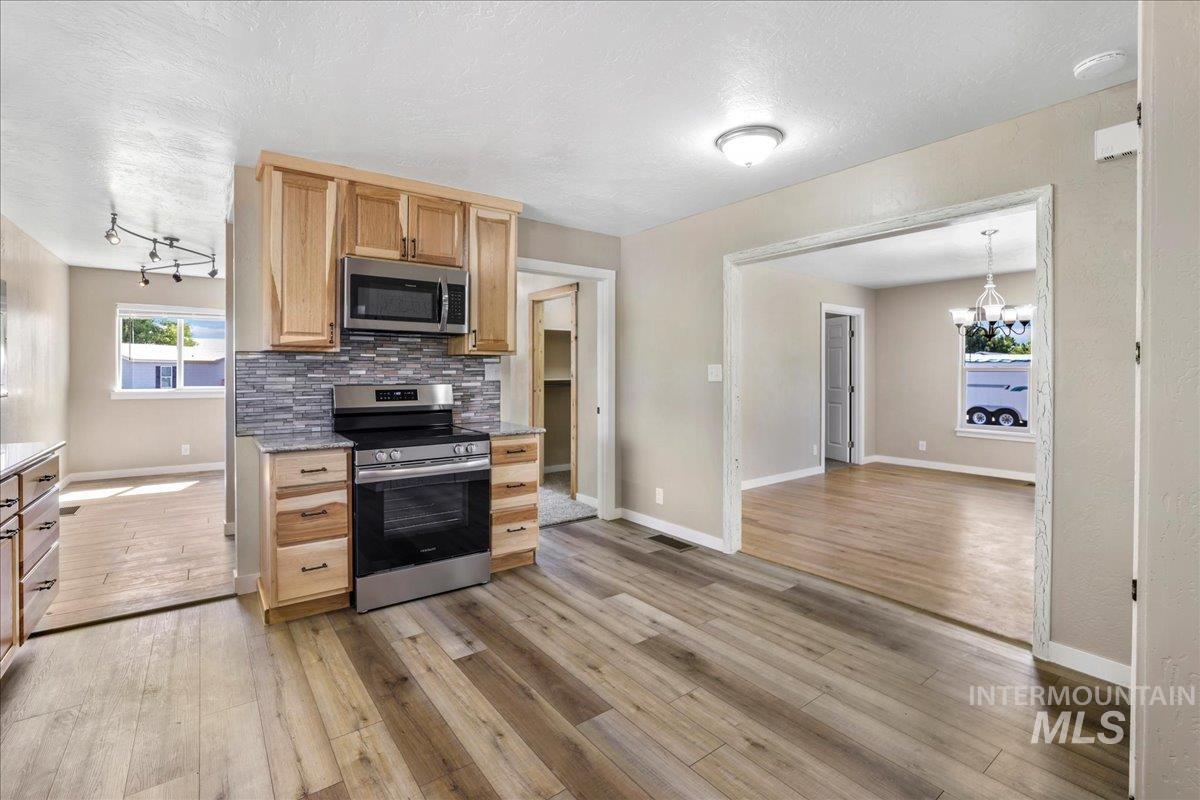 Kitchen with appliances with stainless steel finishes, light brown cabinets, decorative backsplash, light wood finished floors, and a textured ceiling
