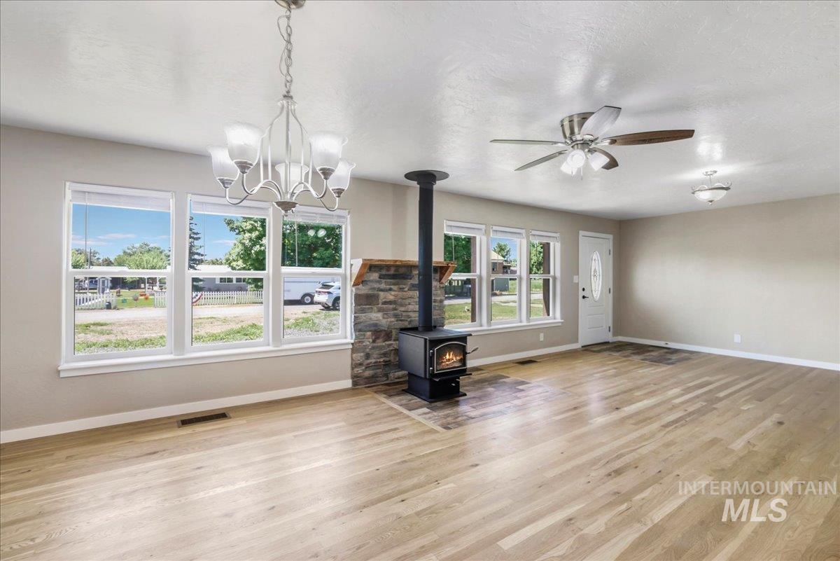 Unfurnished living room featuring a wood stove, light wood-type flooring, a chandelier, and a ceiling fan