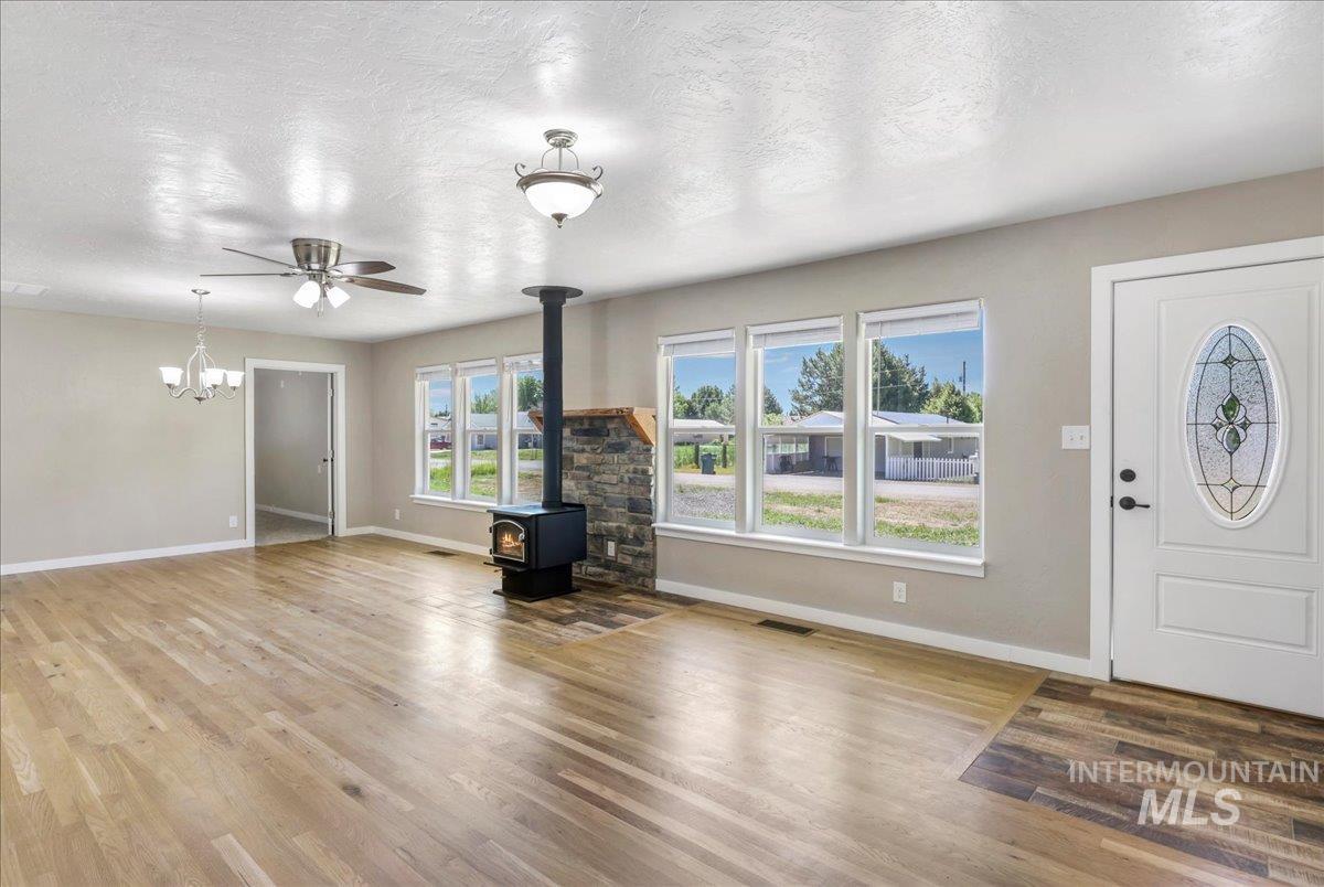 Foyer entrance with a wood stove, wood finished floors, a chandelier, a ceiling fan, and a textured ceiling