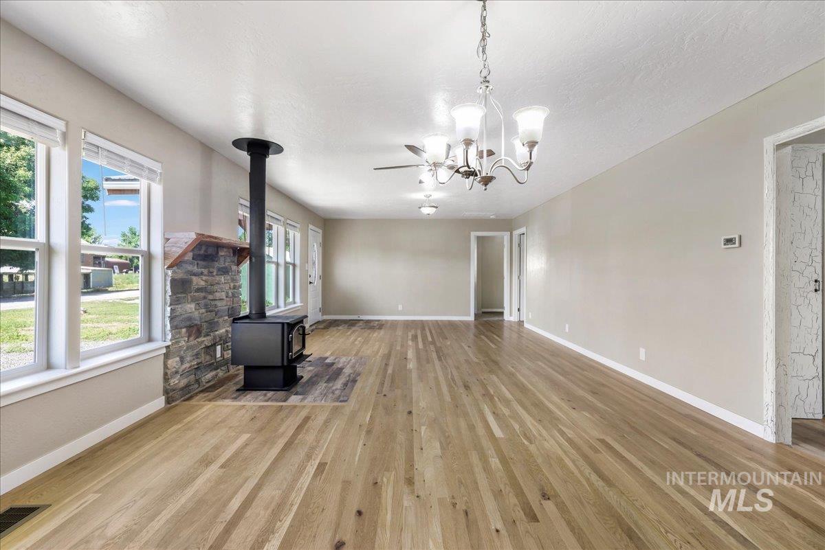 Unfurnished living room featuring a wood stove, wood finished floors, and a chandelier