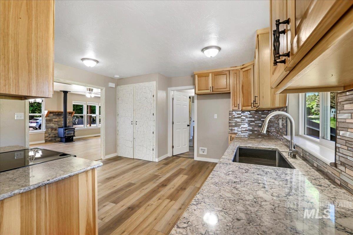 Kitchen with a wood stove, tasteful backsplash, light stone countertops, light brown cabinetry, and light wood-type flooring