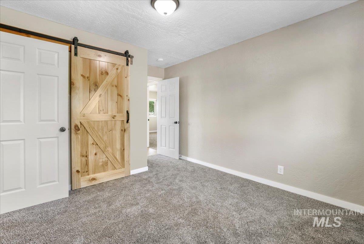 Unfurnished bedroom featuring carpet floors, a barn door, and a textured ceiling