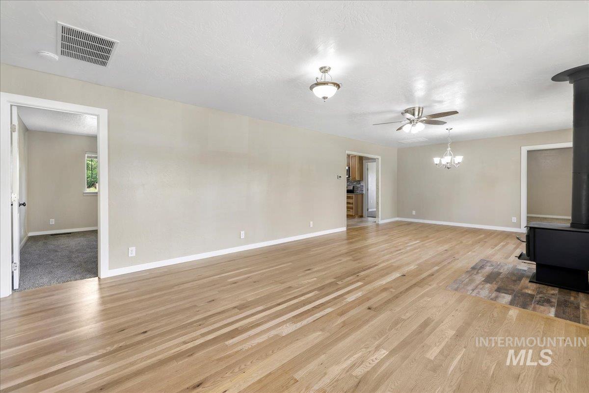 Unfurnished living room featuring a wood stove, light wood-type flooring, ceiling fan, and a chandelier