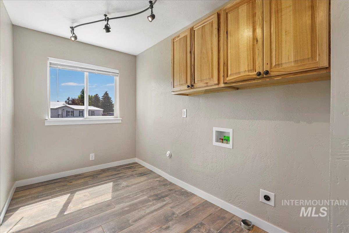 Laundry area featuring hookup for an electric dryer, hookup for a washing machine, cabinet space, wood finished floors, and track lighting