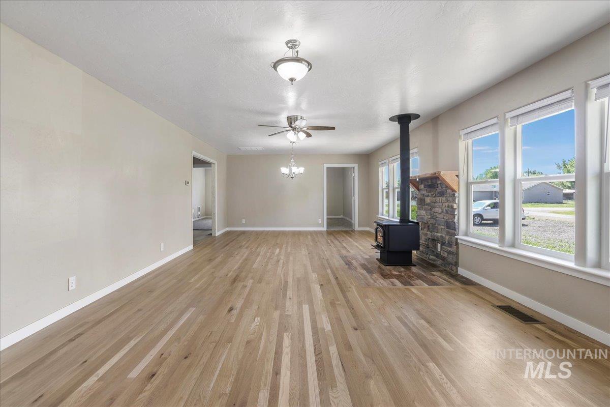 Unfurnished living room with a wood stove, light wood-style floors, ceiling fan, and a chandelier