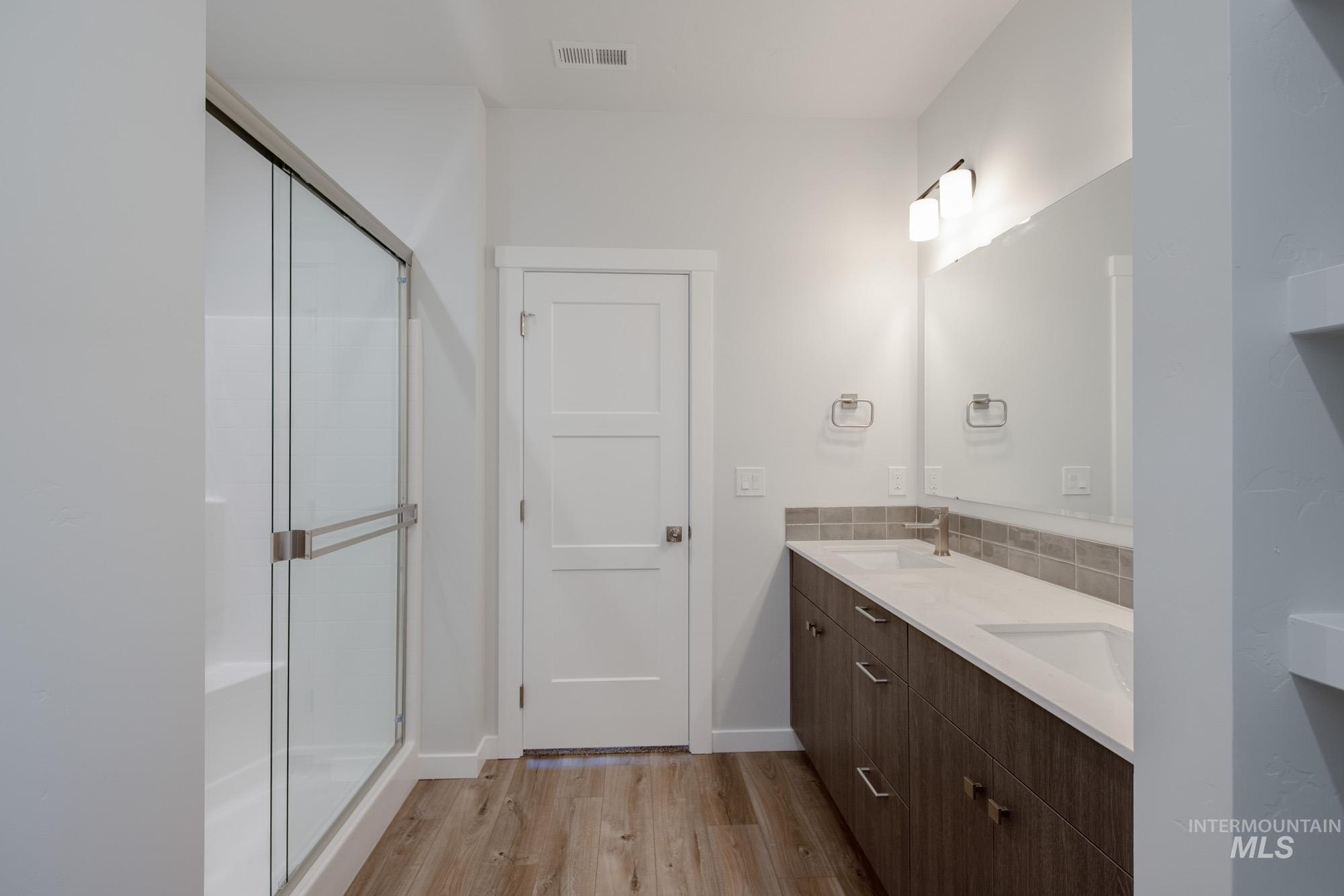 Full bathroom featuring light wood finished floors, double vanity, and a shower stall