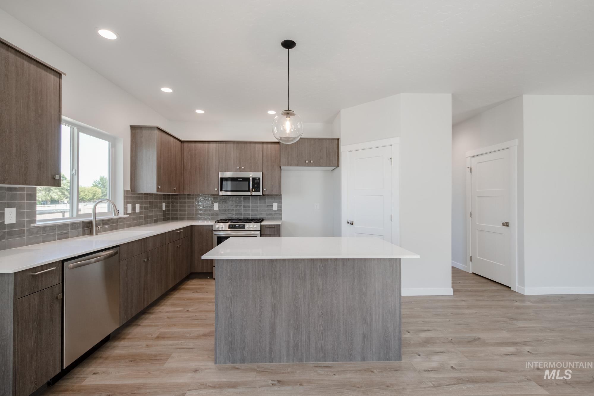 Kitchen with backsplash, modern cabinets, appliances with stainless steel finishes, decorative light fixtures, and light wood finished floors