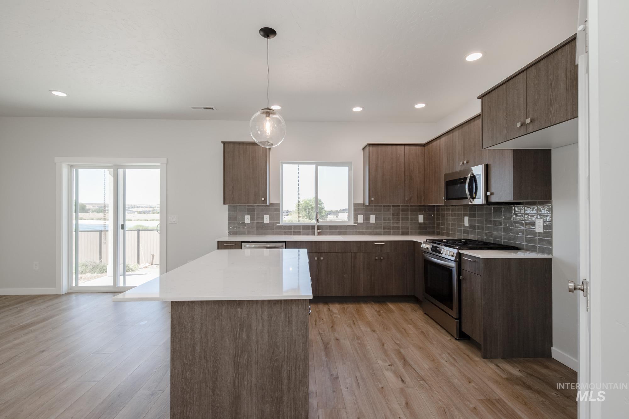 Kitchen featuring stainless steel appliances, decorative light fixtures, tasteful backsplash, light wood finished floors, and a kitchen island