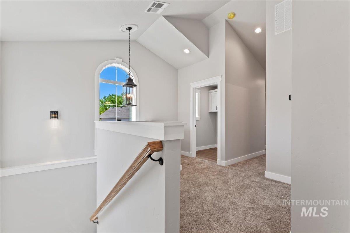 Hallway featuring light carpet, vaulted ceiling, recessed lighting, and an upstairs landing