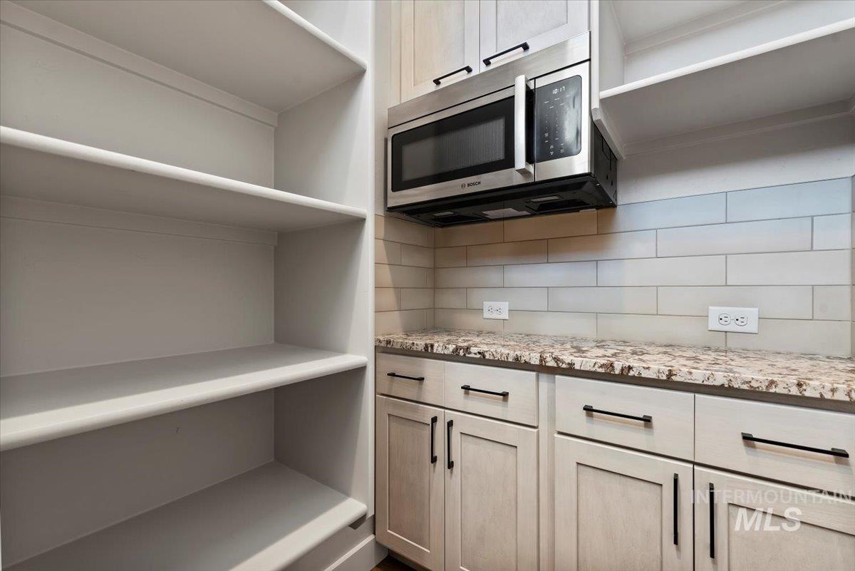Kitchen Pantry featuring stainless steel microwave, tasteful backsplash, open shelves, and light stone counters