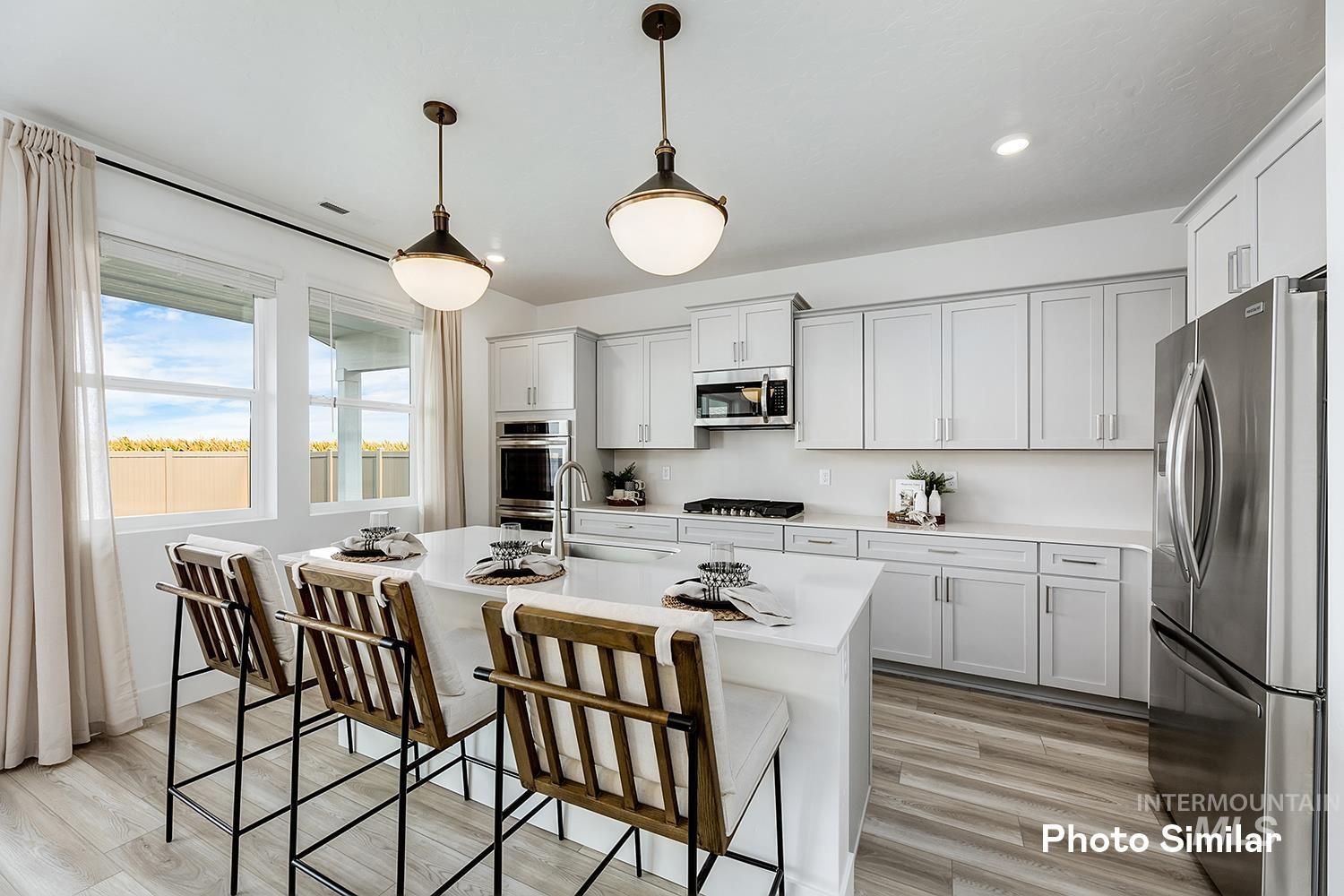 Kitchen featuring stainless steel appliances, light wood finished floors, a kitchen breakfast bar, an island with sink, and decorative light fixtures