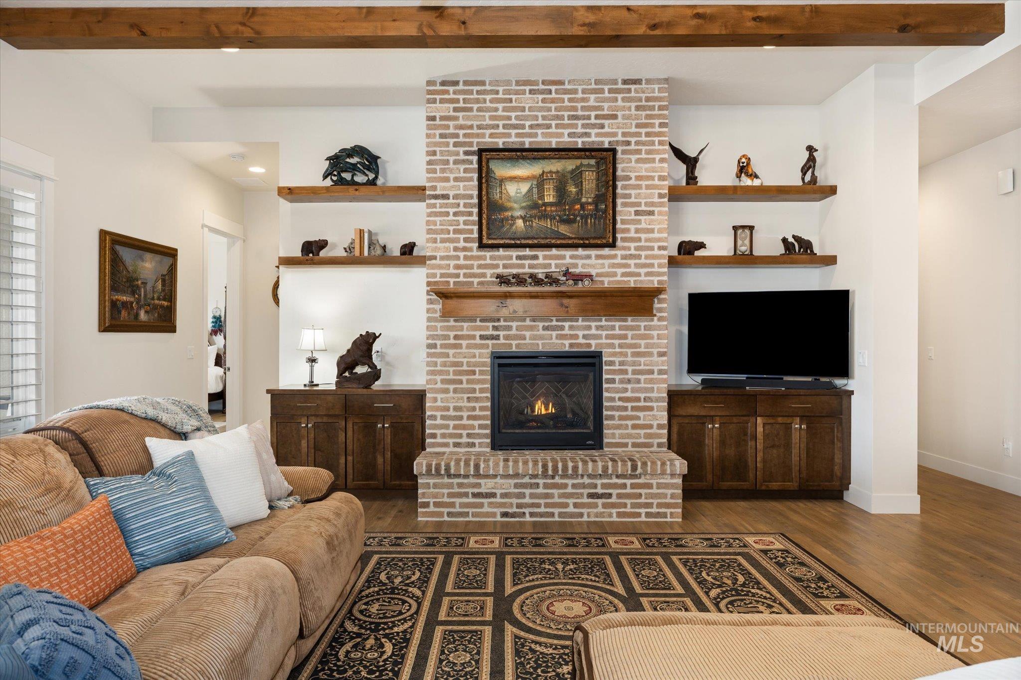 Living room with beam ceiling, a brick fireplace, and dark wood-style flooring