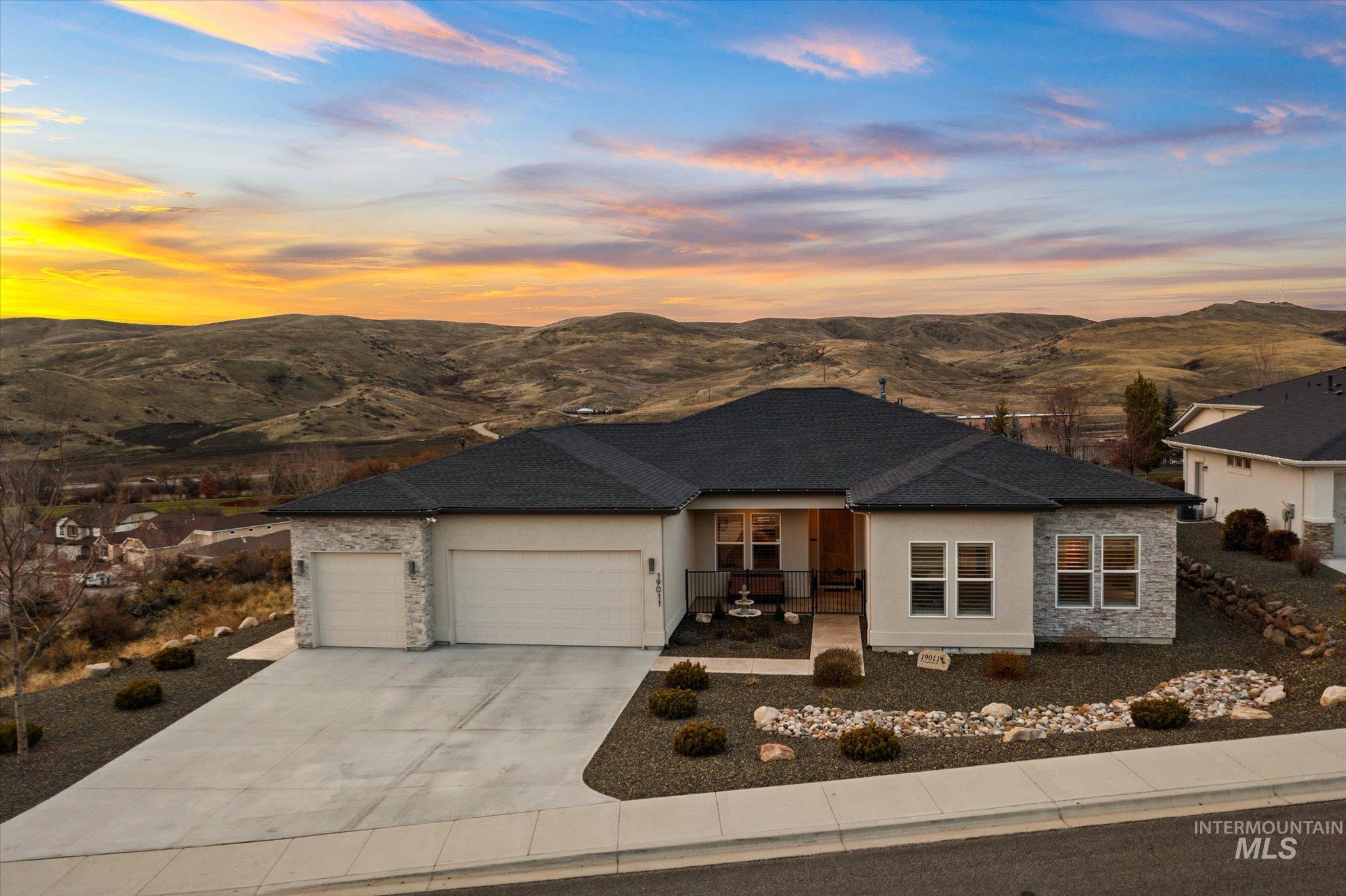View of front of home featuring stone siding, an attached garage, a mountain view, stucco siding, and concrete driveway