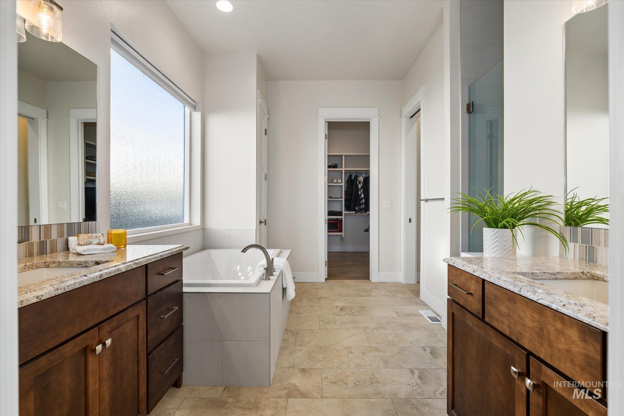Full bathroom featuring a spacious closet, two vanities, a garden tub, and recessed lighting