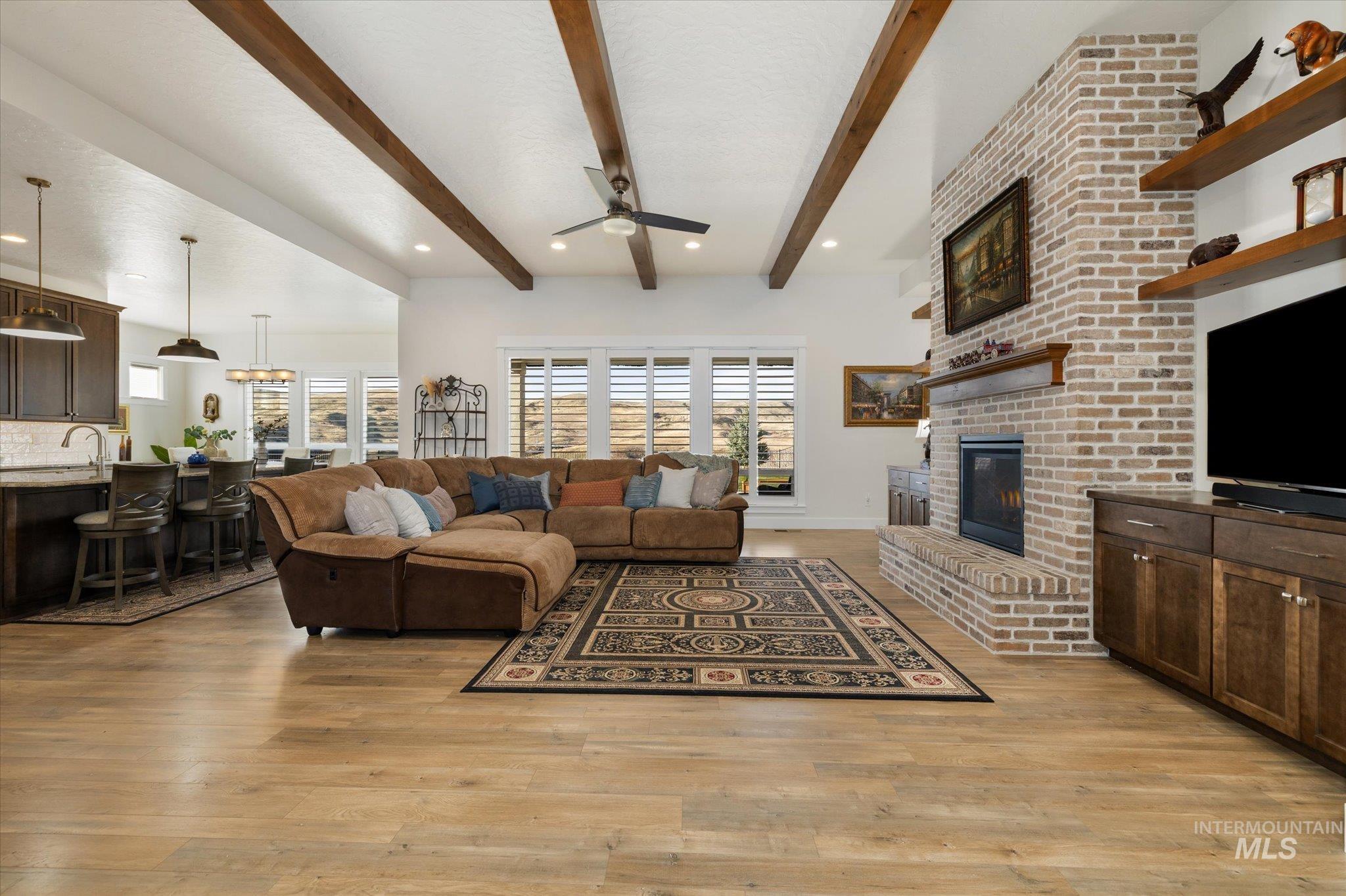 Living area with a brick fireplace, ceiling fan, plenty of natural light, beamed ceiling, and recessed lighting