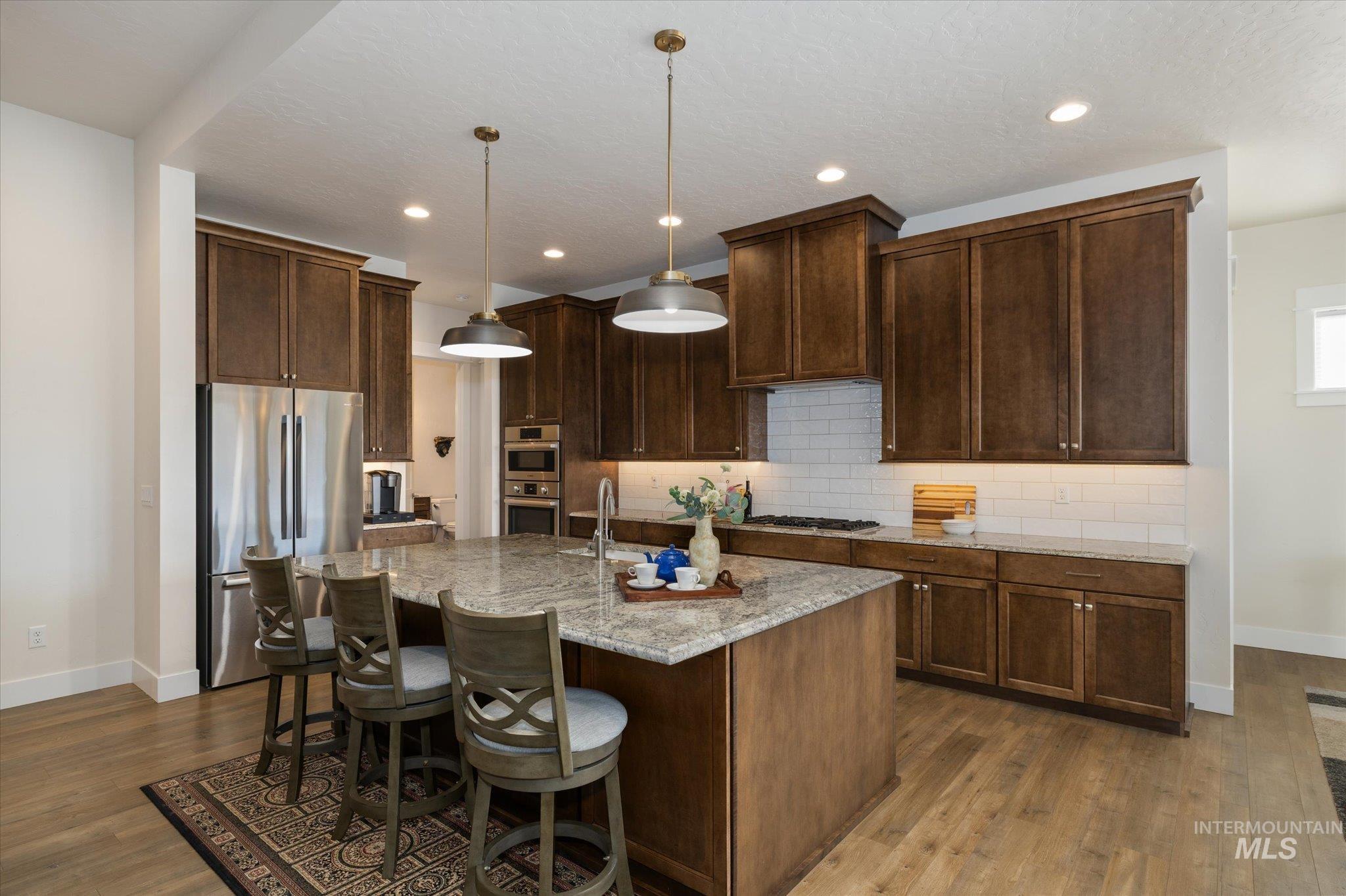 Kitchen featuring stainless steel appliances, decorative light fixtures, light stone counters, a breakfast bar area, and a kitchen island with sink
