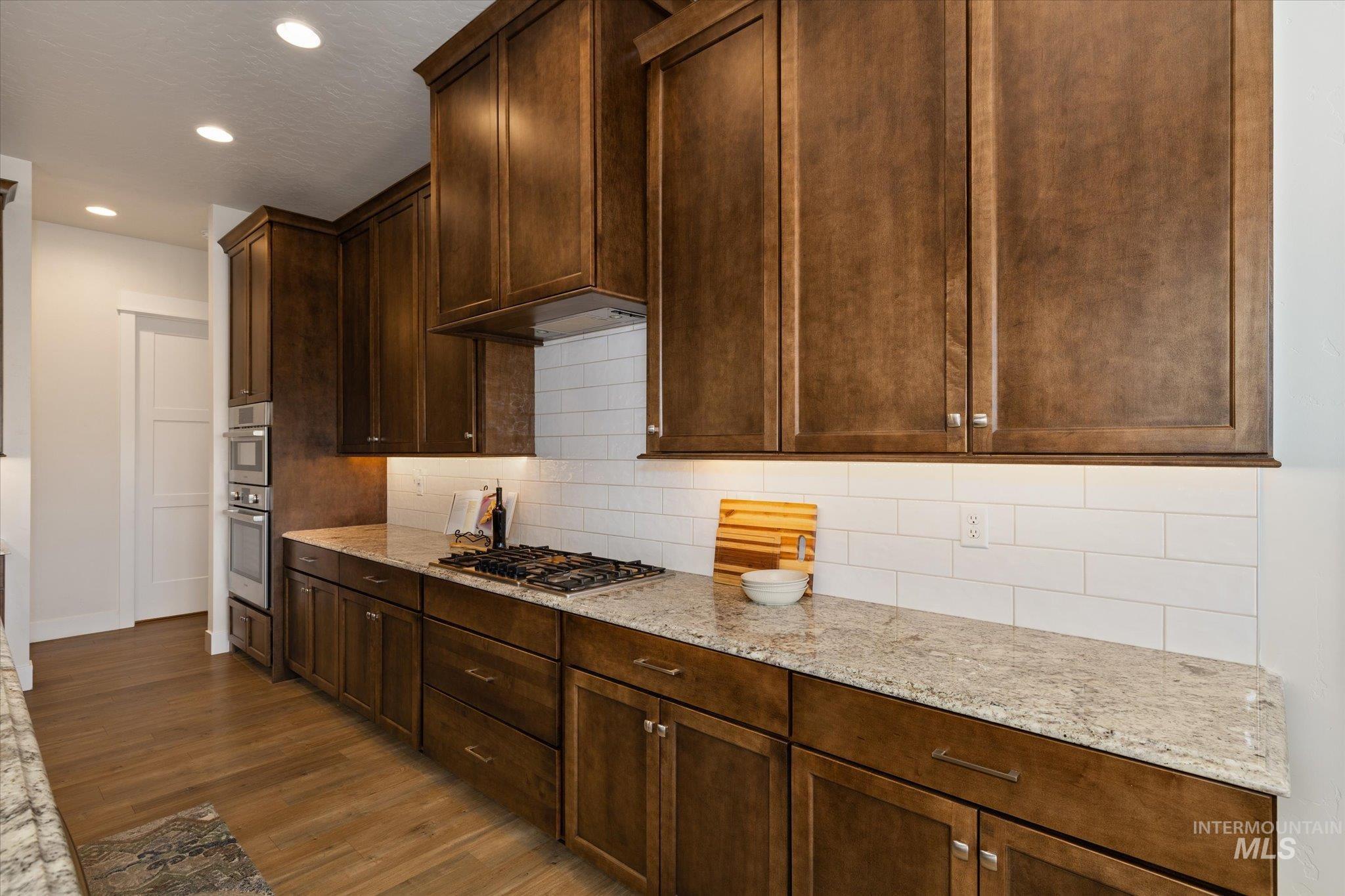 Kitchen featuring light stone counters, dark wood-style flooring, tasteful backsplash, recessed lighting, and stainless steel appliances