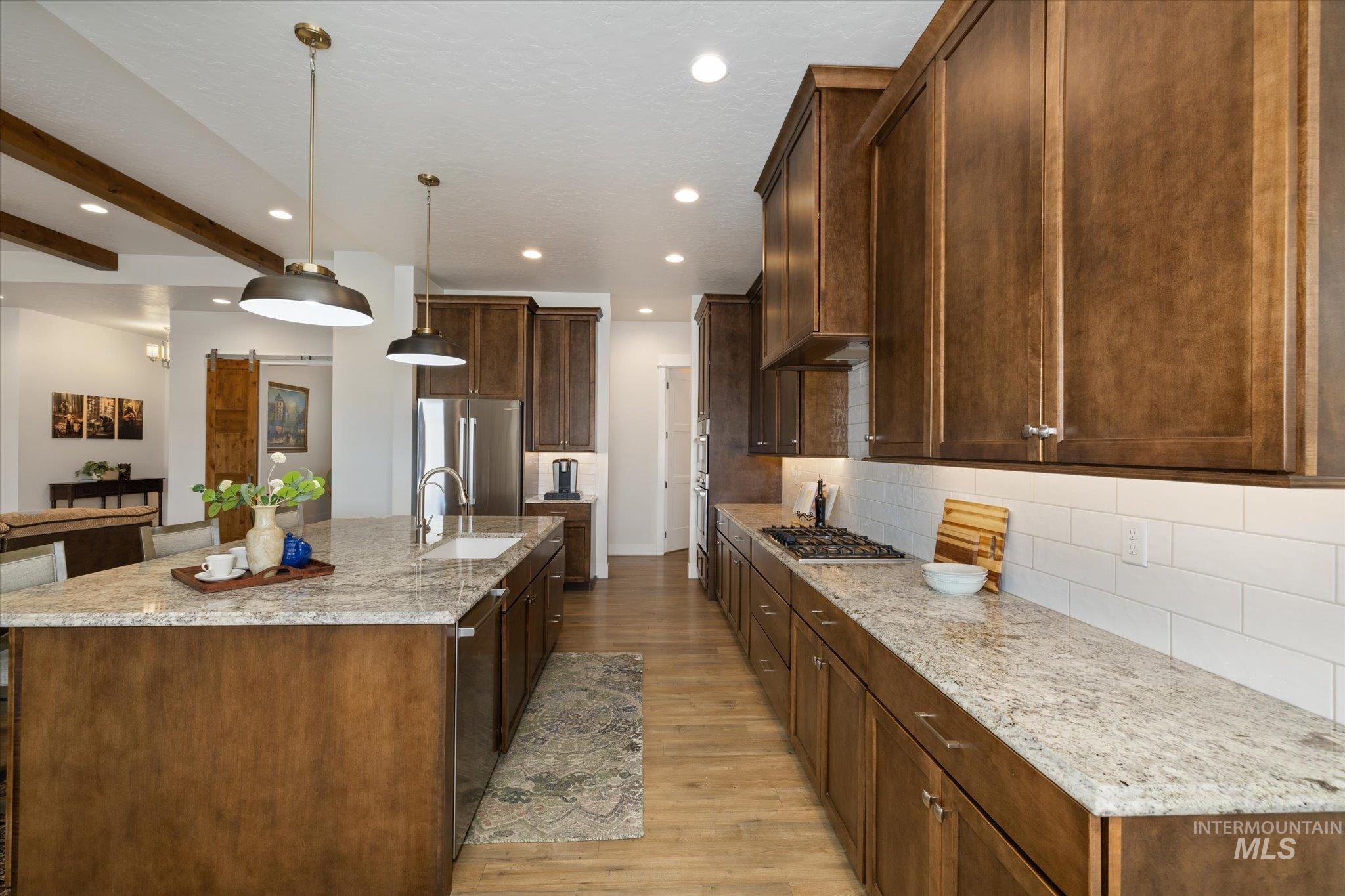 Kitchen with hanging light fixtures, light stone counters, light wood-style flooring, recessed lighting, and a center island with sink