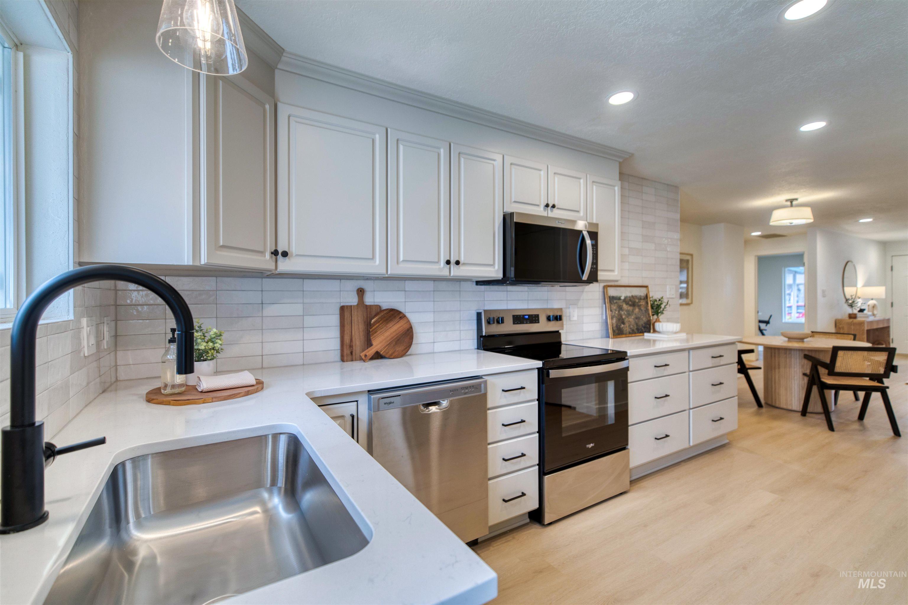 Kitchen with appliances with stainless steel finishes, white cabinets, light wood-style floors, pendant lighting, and recessed lighting