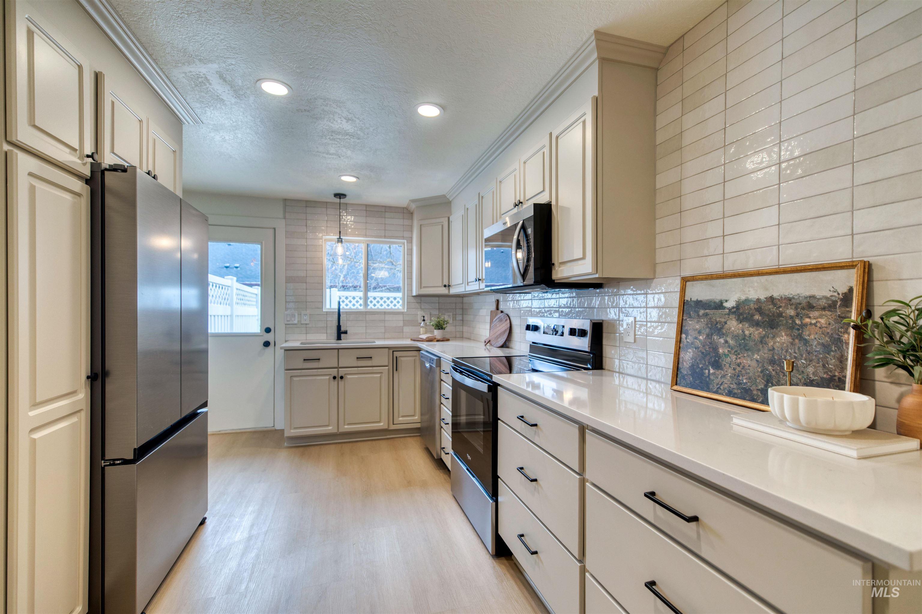 Kitchen featuring stainless steel appliances, a textured ceiling, tasteful backsplash, pendant lighting, and light wood finished floors
