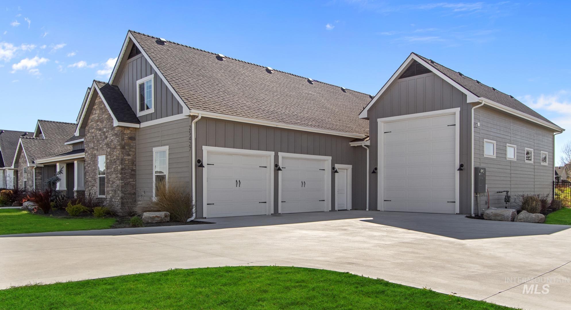View of property exterior with roof with shingles, board and batten siding, driveway, and stone siding