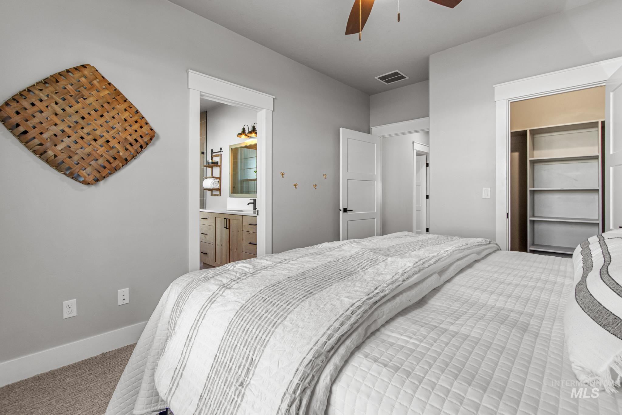 Bedroom with carpet floors, a ceiling fan, a walk in closet, and ensuite bath