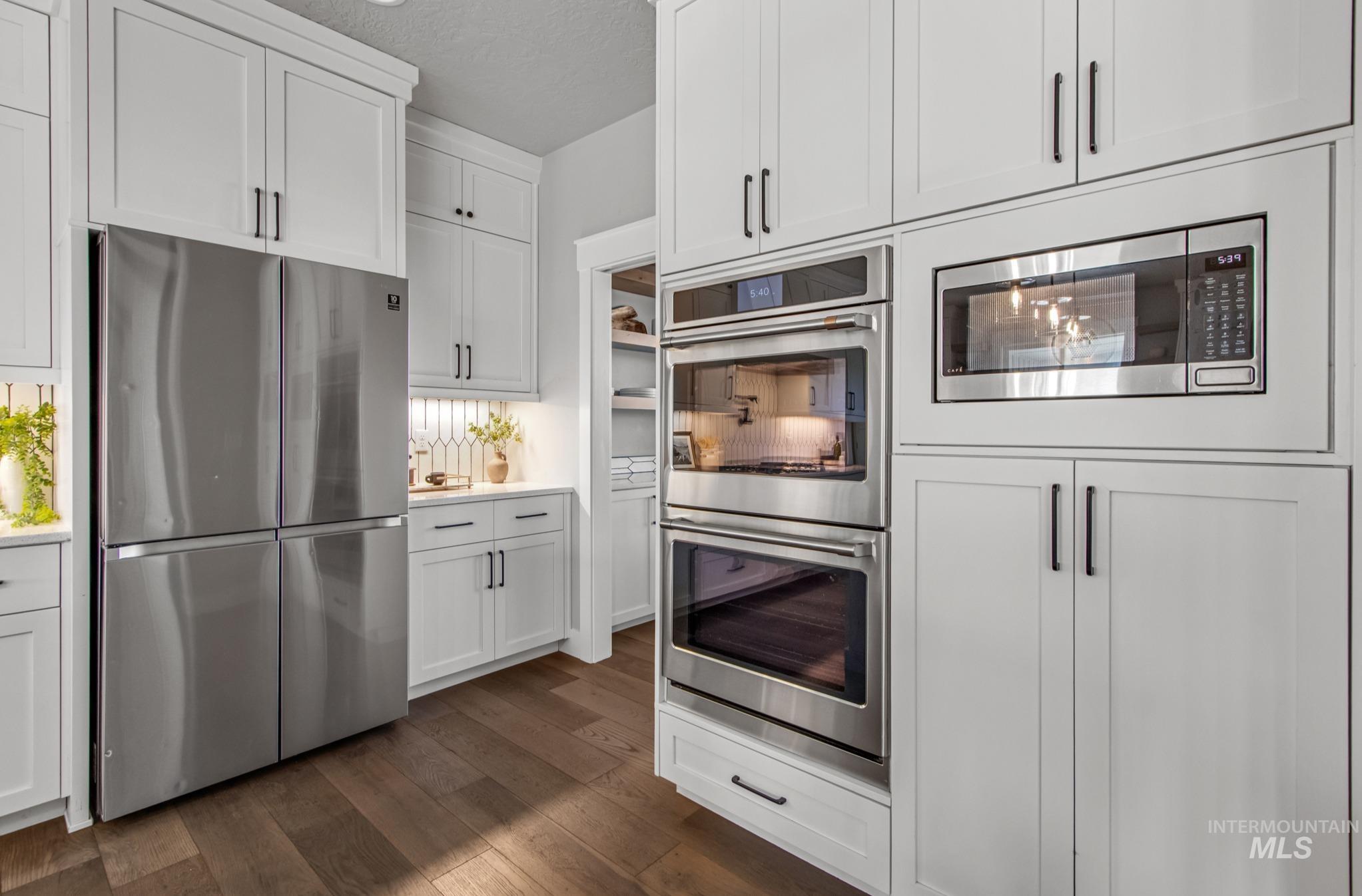 Kitchen with stainless steel appliances, a textured ceiling, white cabinets, and dark wood-style floors