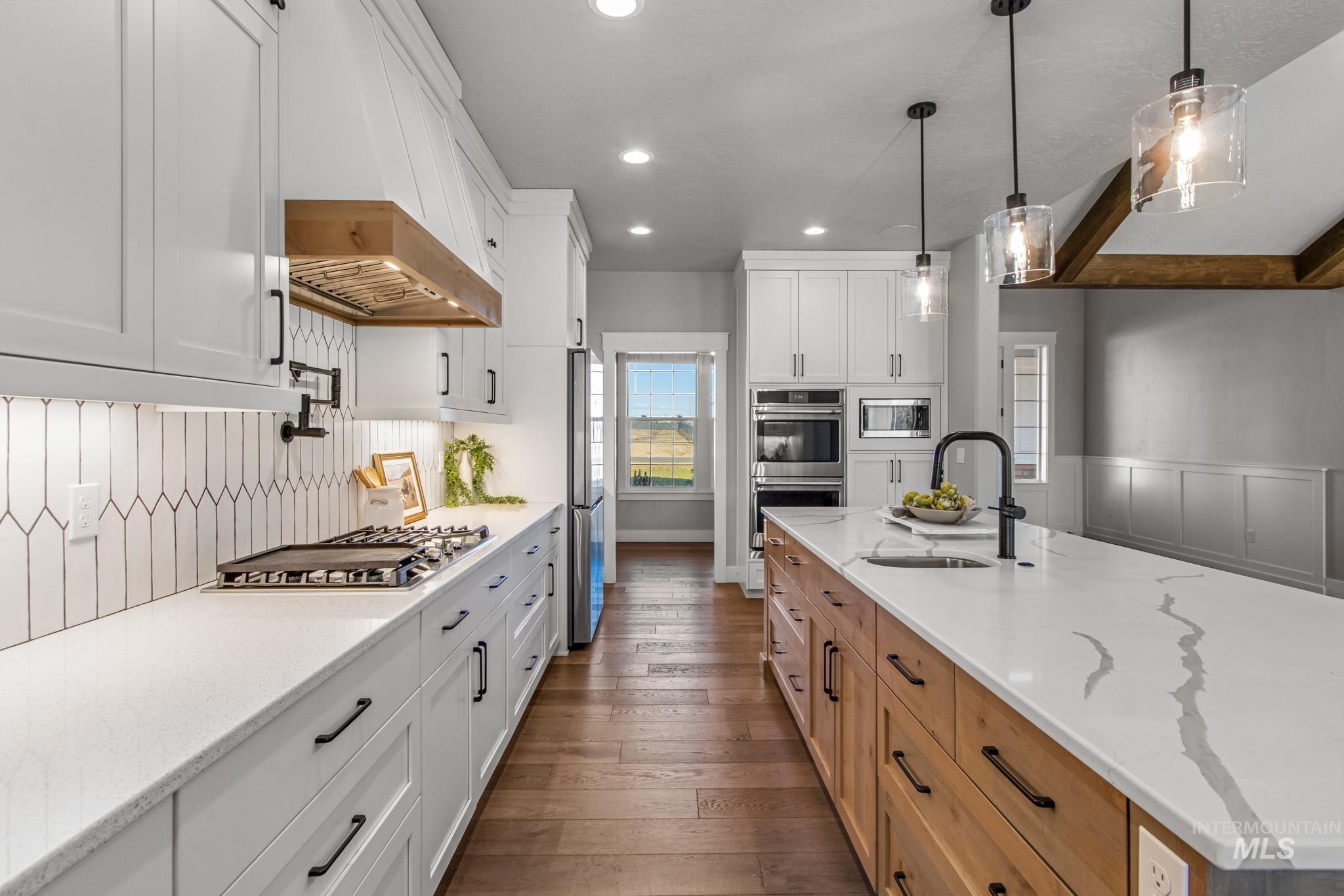 Two tone kitchen featuring two tone color scheme, light stone counters, stainless steel appliances, pendant lighting, and a decorative wall