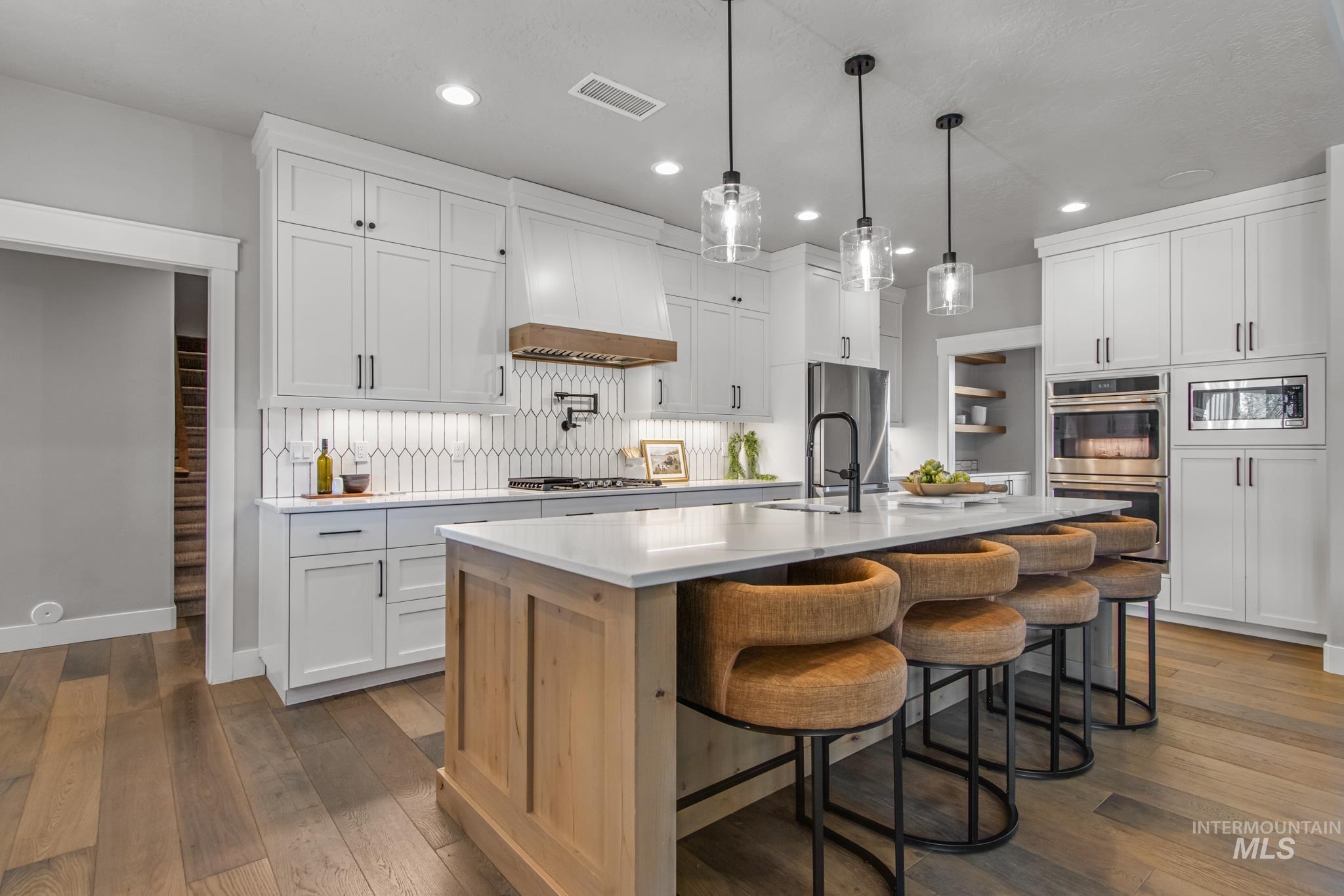 Kitchen with stainless steel appliances, a breakfast bar, a kitchen island with sink, hanging light fixtures, and dark wood-style flooring