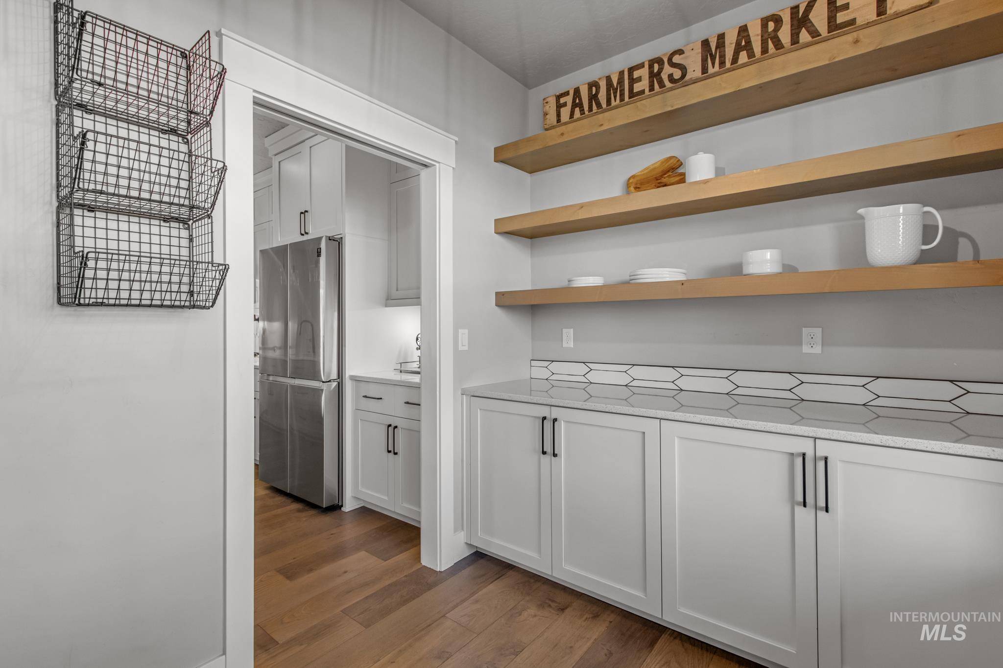 Kitchen with light stone countertops, freestanding refrigerator, open shelves, dark wood-type flooring, and white cabinets